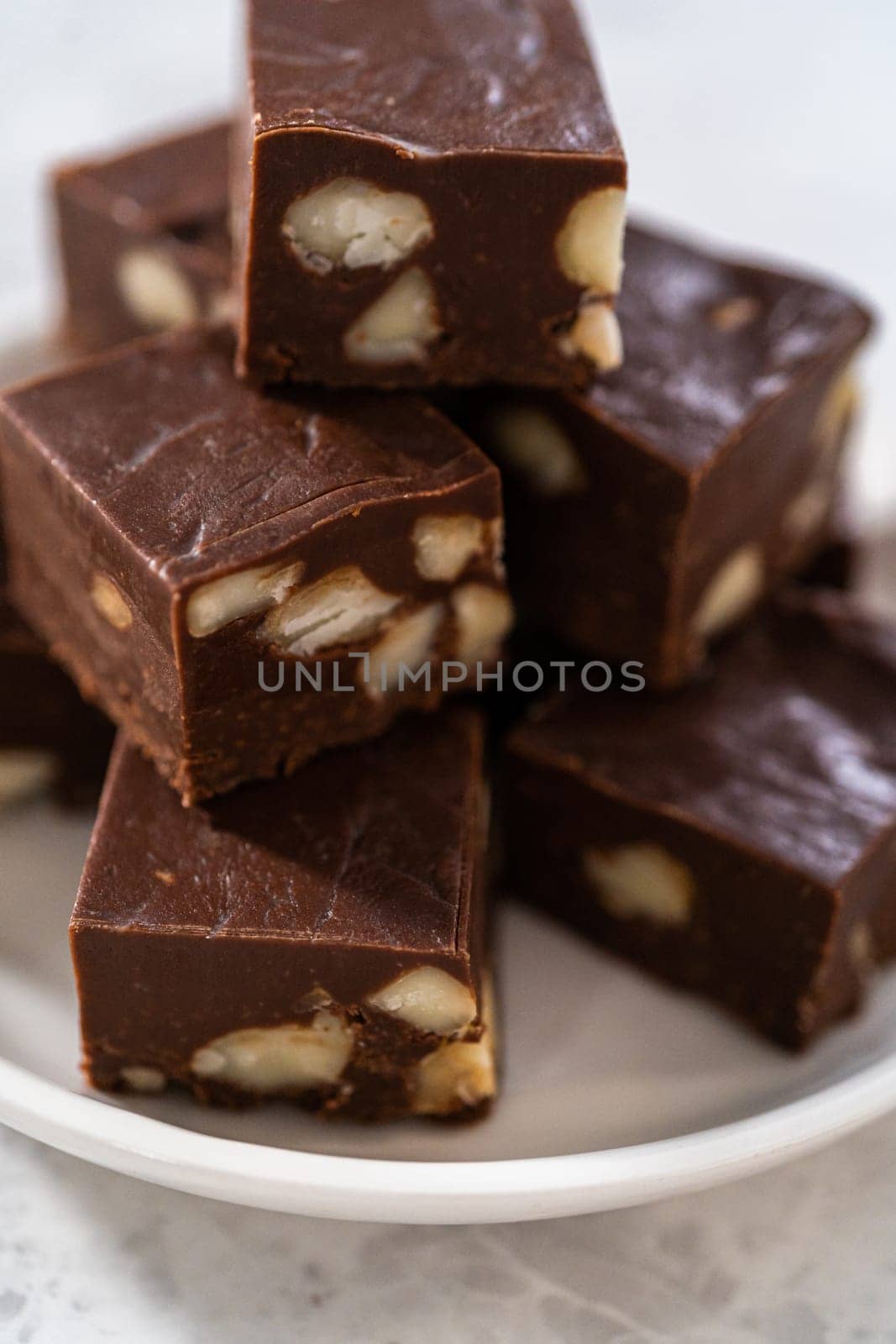 Homemade chocolate macadamia fudge square pieces on a white plate.