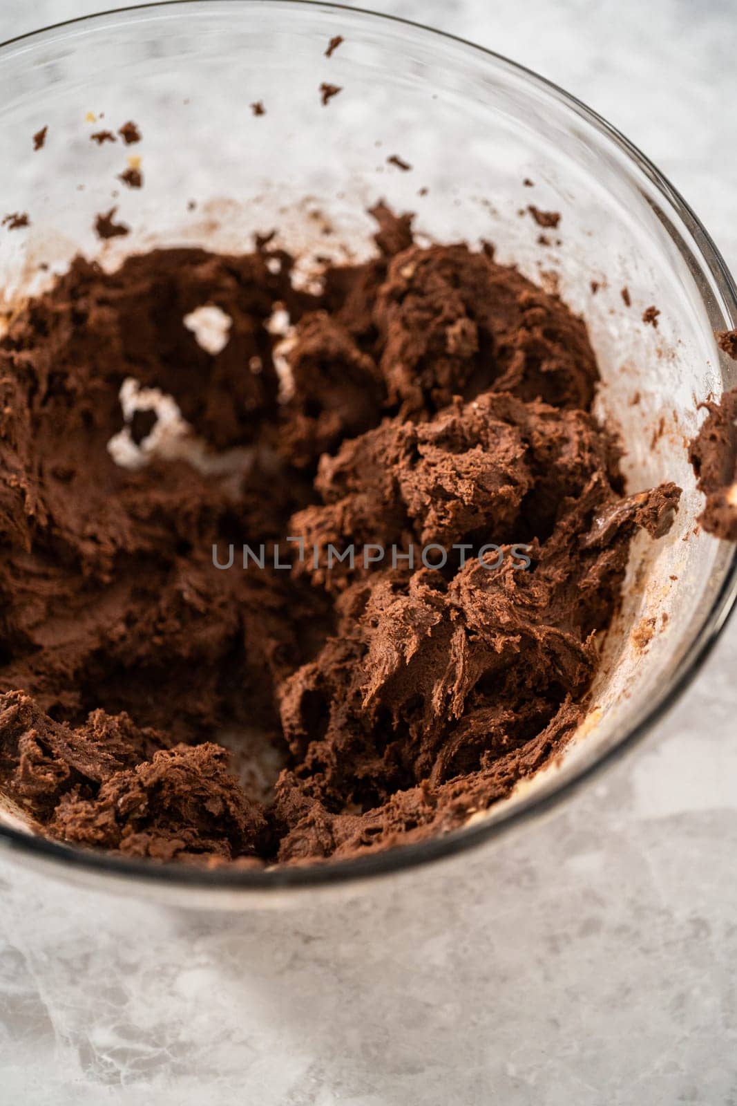 Mixing ingredients in a large glass mixing bowl with a kitchen mixer to bake chocolate cookies with peppermint chips.