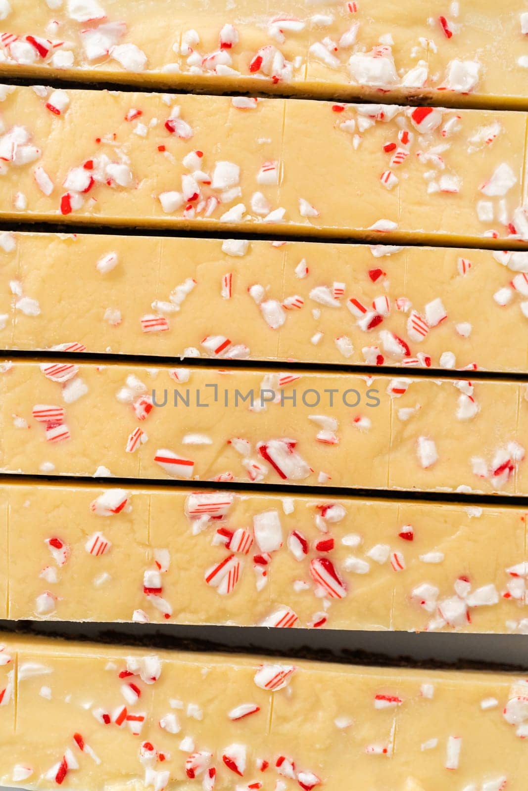 Cutting candy cane fudge with a large kitchen knife into square pieces on a white cutting board.