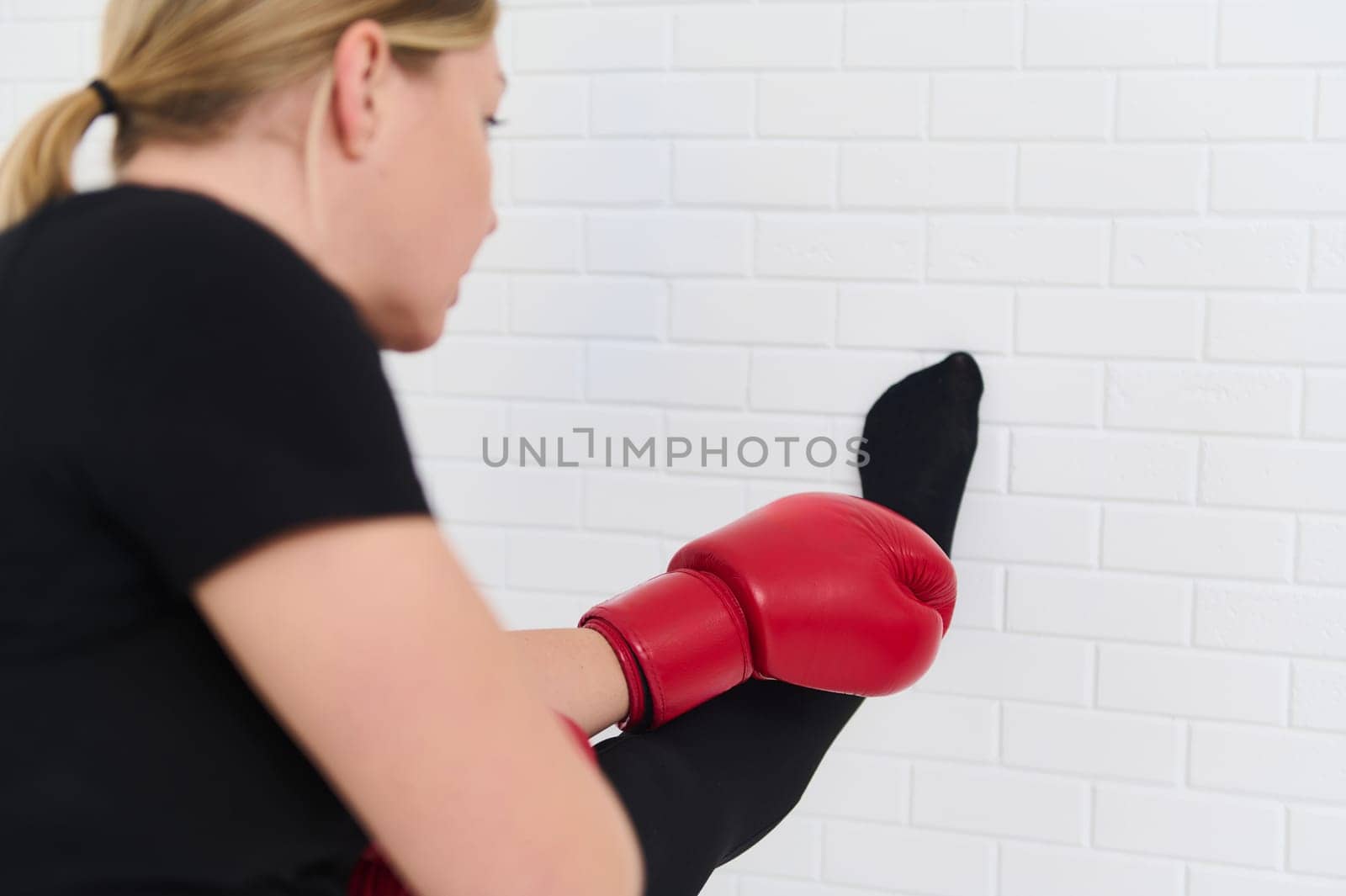 Female boxer stretching arms, warming up her body before boxing training, wearing boxing gloves, isolated over white studio background