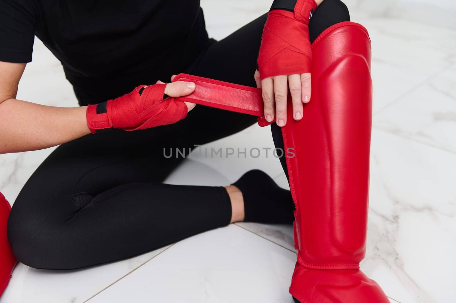Selective focus on legs of a woman boxer fighter putting on red kickboxing leg pads guard. Sparring shin guards. Martial art, combat, challenge. Kickboxing concept
