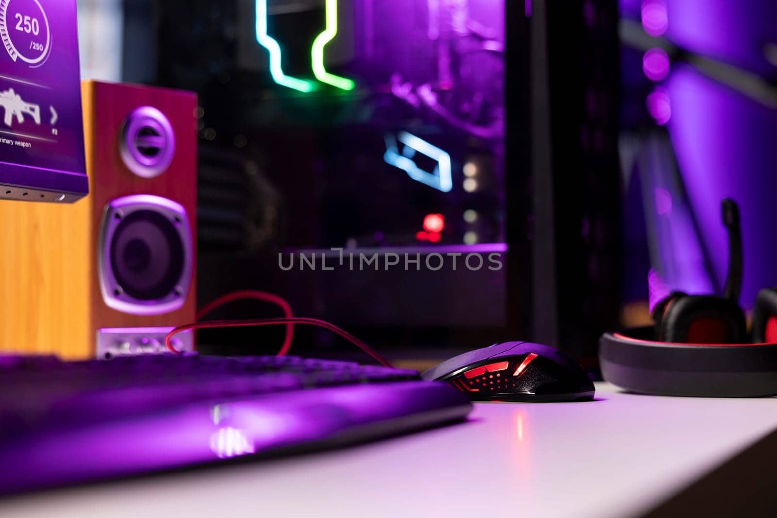 Neon lit components on opened gaming PC device next to keyboard, speakers, wired mouse and headphones in empty apartment. Computer in home with colorful gpu and cpu parts, close up shot