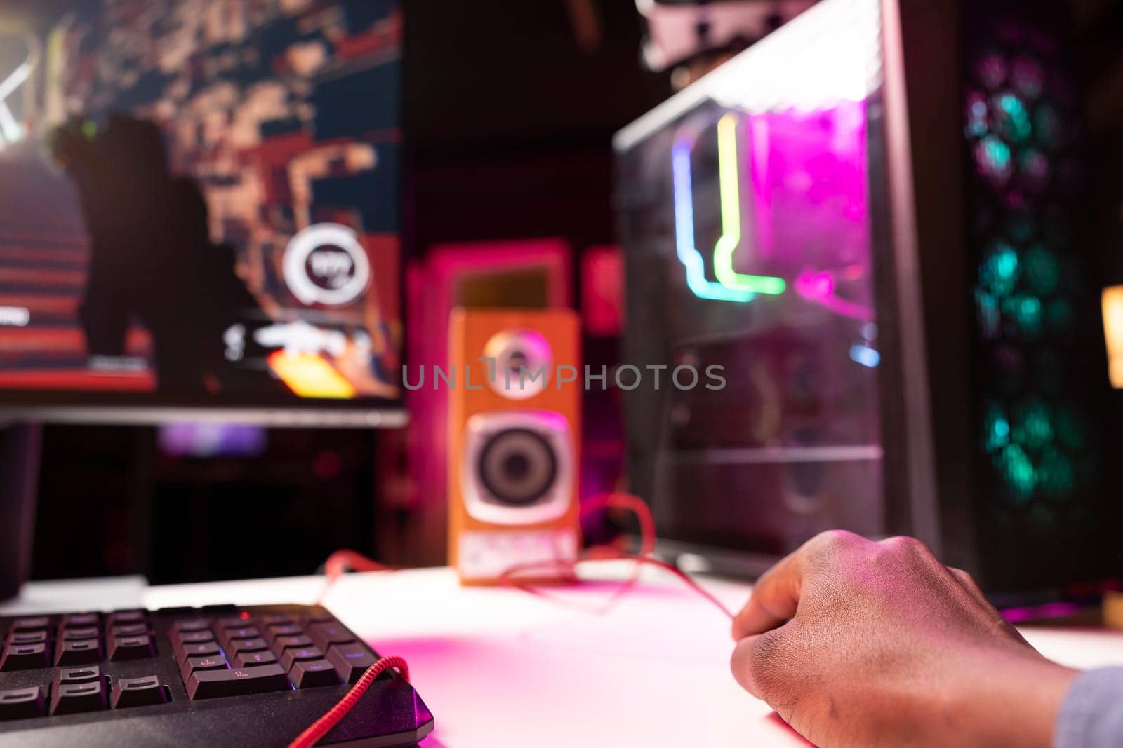 Gamer using keyboard and mouse to play FPS videogame on gaming PC tower with neon lit components. Man in apartment at night using high tech computer peripherals to defeat foes, close up