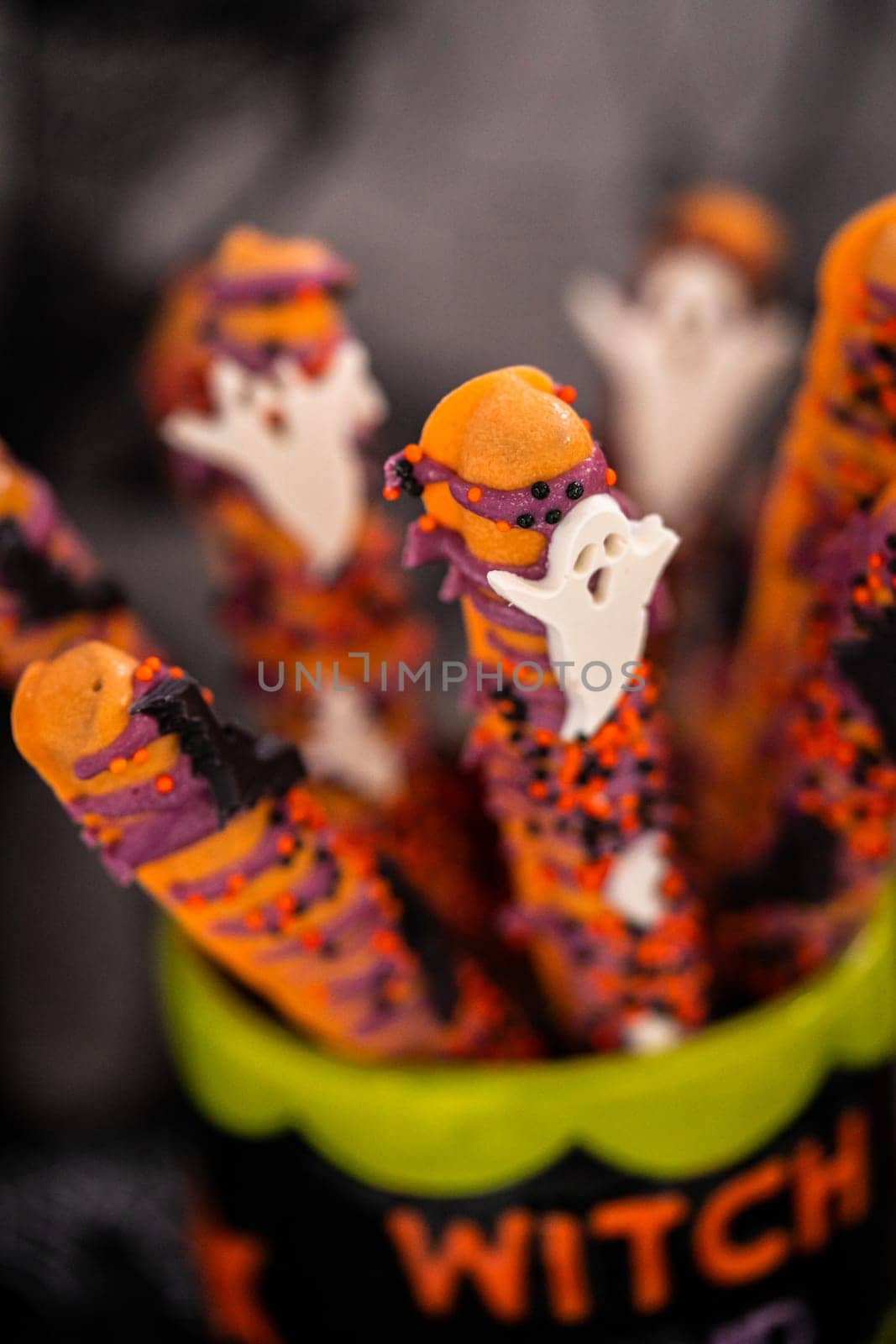 Halloween chocolate-covered pretzel rods with sprinkles in a cup.