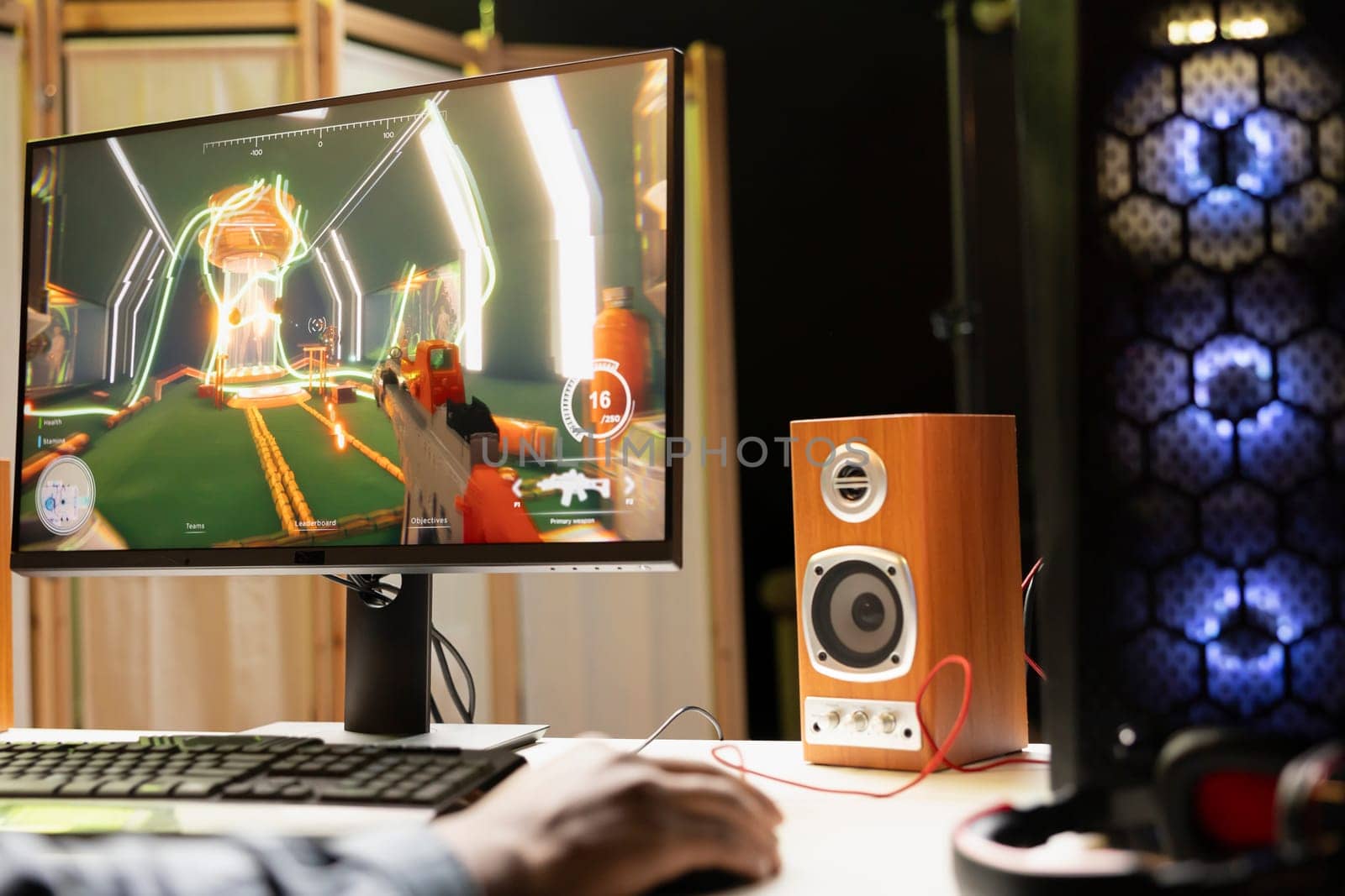 Man in RGB lit apartment playing first person shooter videogame on desktop PC at computer desk, unwinding. BIPOC player competing against enemies in internet multiplayer FPS