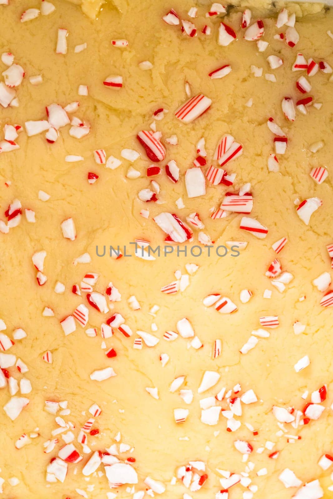 Filling square cheesecake pan lined with parchment paper with fudge mixture to prepare candy cane fudge.