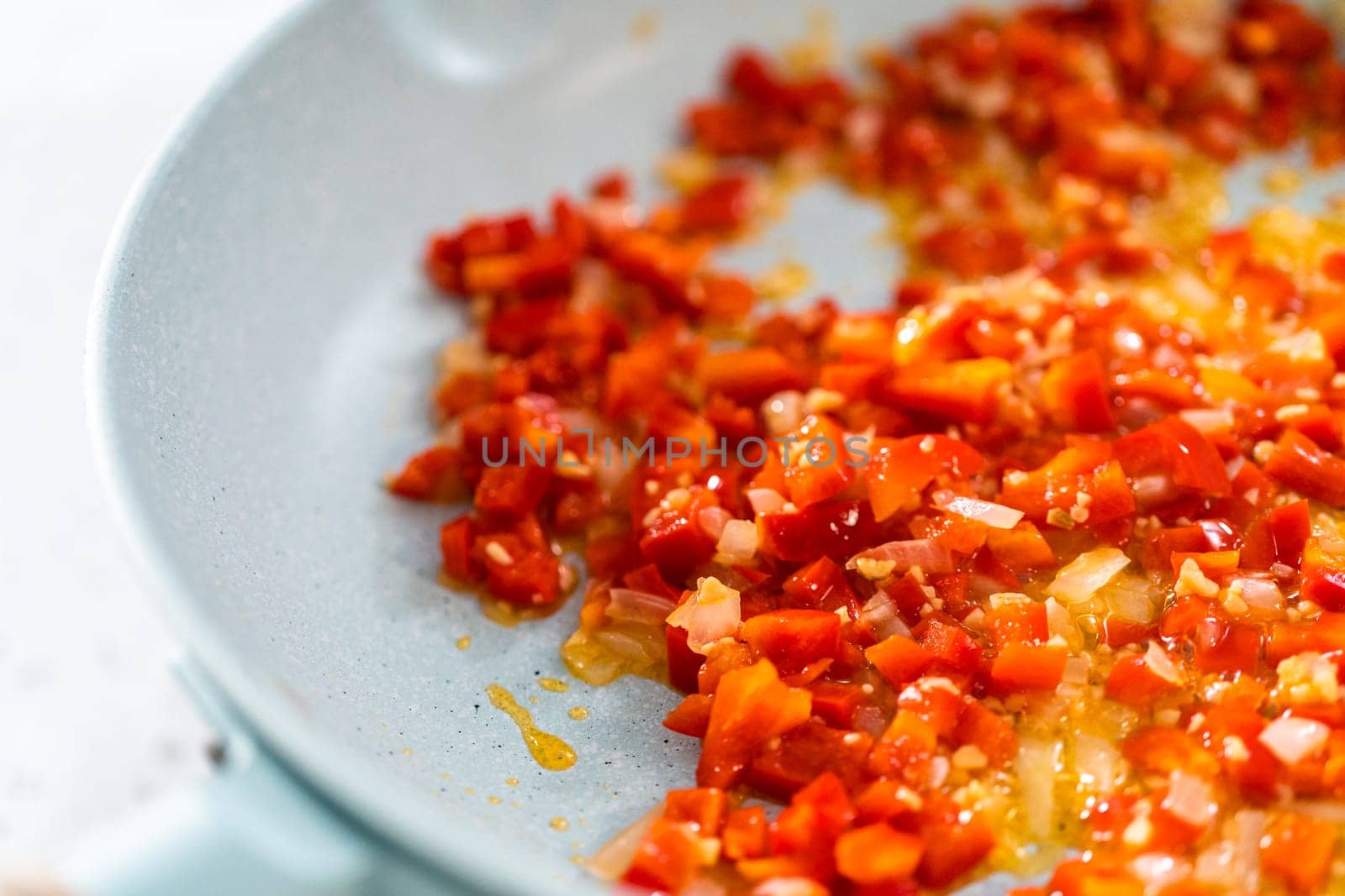 Frying onion and red bell pepper in olive oil on a nonstick frying pan to bake turkey empanadas.