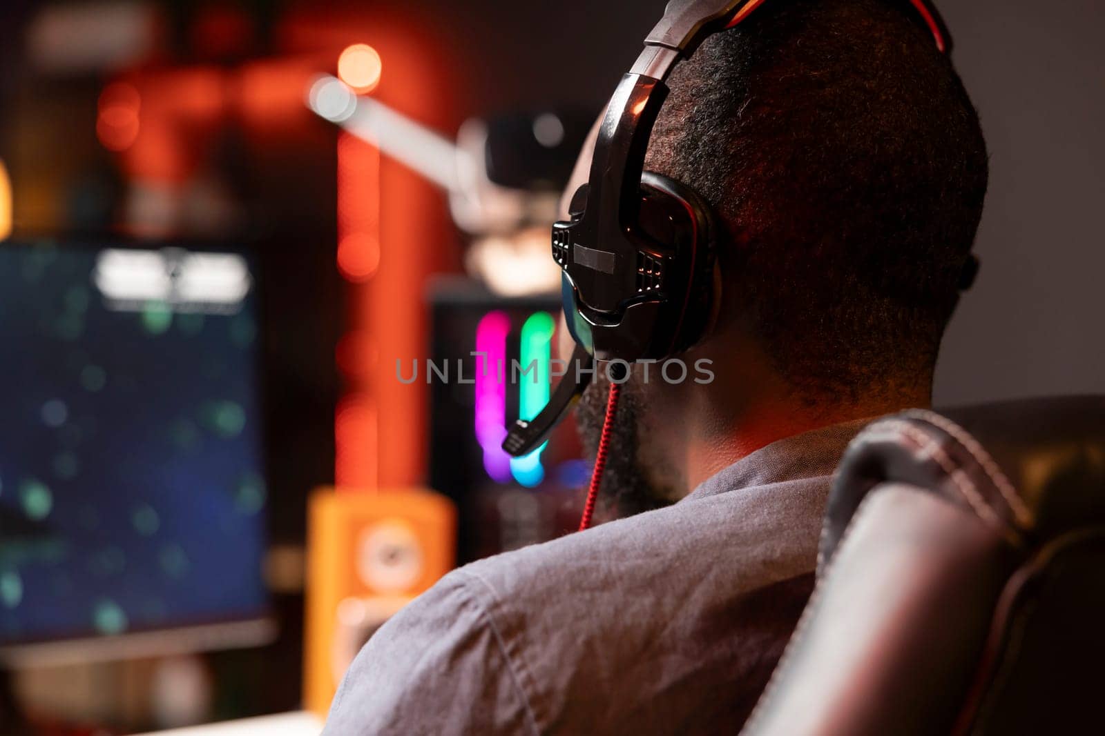 Player using headphones to discuss with mates while playing online videogame on gaming PC monitor. Man enjoying coop game with friends on computer display, chatting on internet late at night