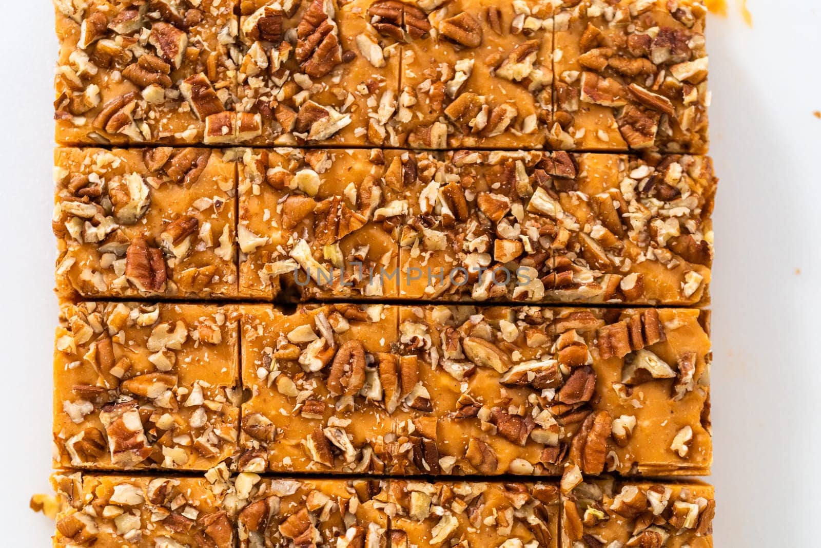 Cutting pumpkin spice fudge into square pieces on a white cutting board.