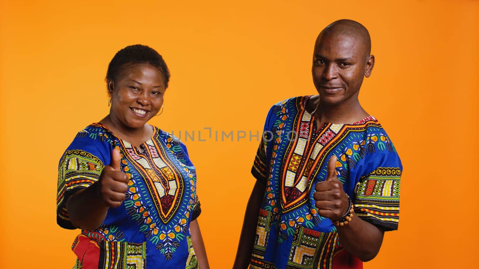 African american partners giving thumbs up gesture in studio, feeling cheerful and presenting their positive feedback. Married couple showing approval and doing like symbol on camera.