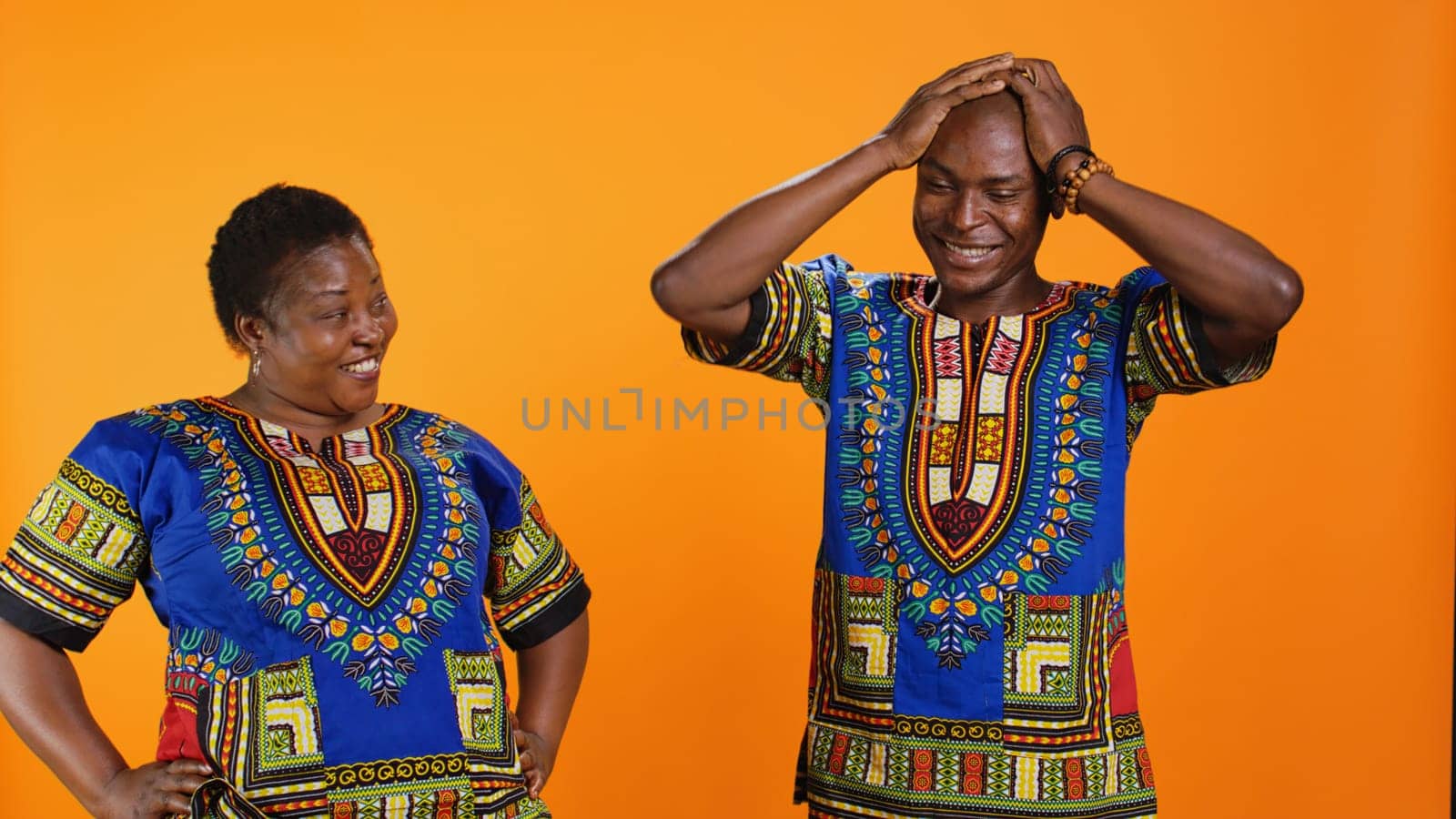 Joyful man and woman laughing together in studio, having fun with silly jokes over orange background. African american people enjoying funny moments with laugh, amused couple.