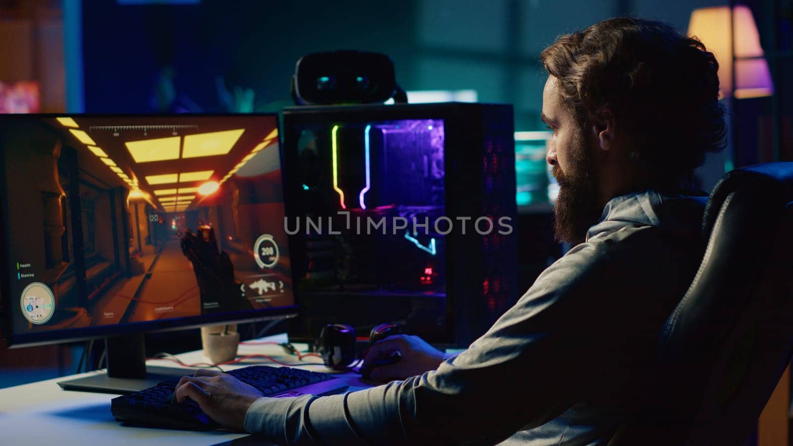 Portrait of smiling man in dimly lit apartment playing video games on gaming PC at computer desk, enjoying day off from work. Gamer battling enemies in online multiplayer shooter