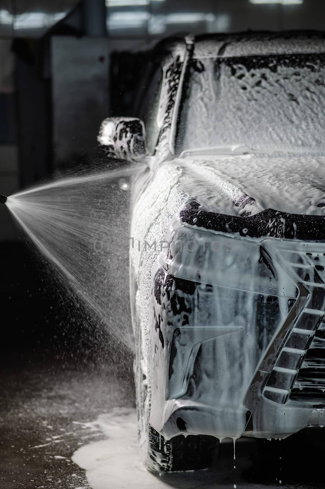 Man applying foam to black car in car wash. Vertical photo