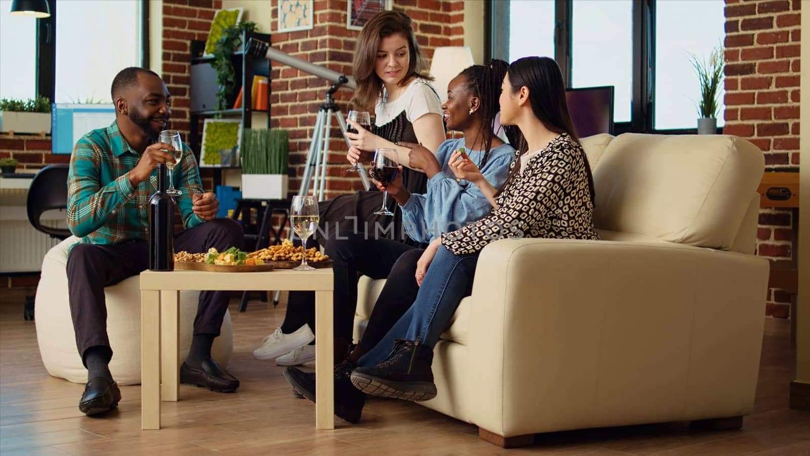 Culturally diverse group of people talking, drinking wine at friends social reunion. African american woman enjoying talking with mates, having fun together, eating snacks