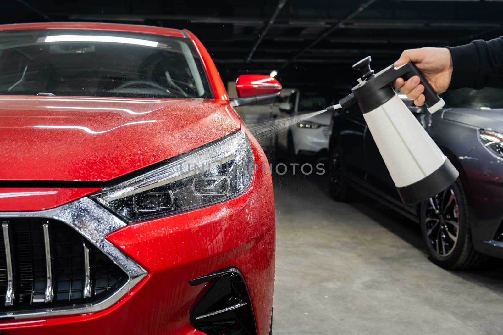 A man washes the headlights of a red car with a spray