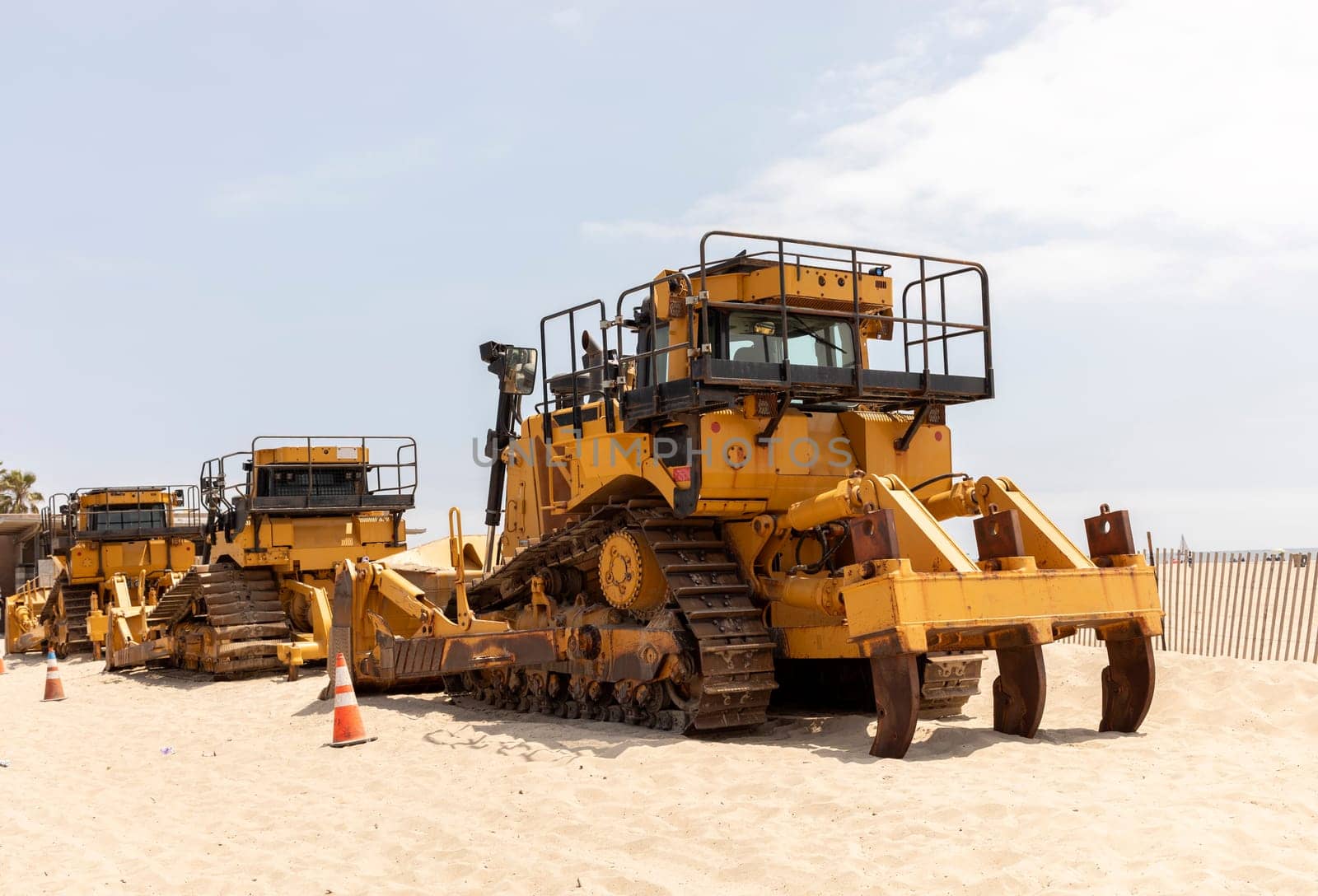 Few Yellow Crawler Dozer On Sandy Beach, Blue Sky On Background. Bulldozer Builds Roads. Construction And Landfill Equipment And Machinery. No People. Horizontal Plane. High quality photo