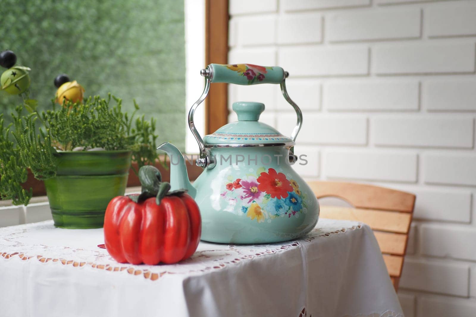 Retro-style teapot, red ceramic pepper, and herb pot on a table with a lace tablecloth in a cozy setting.