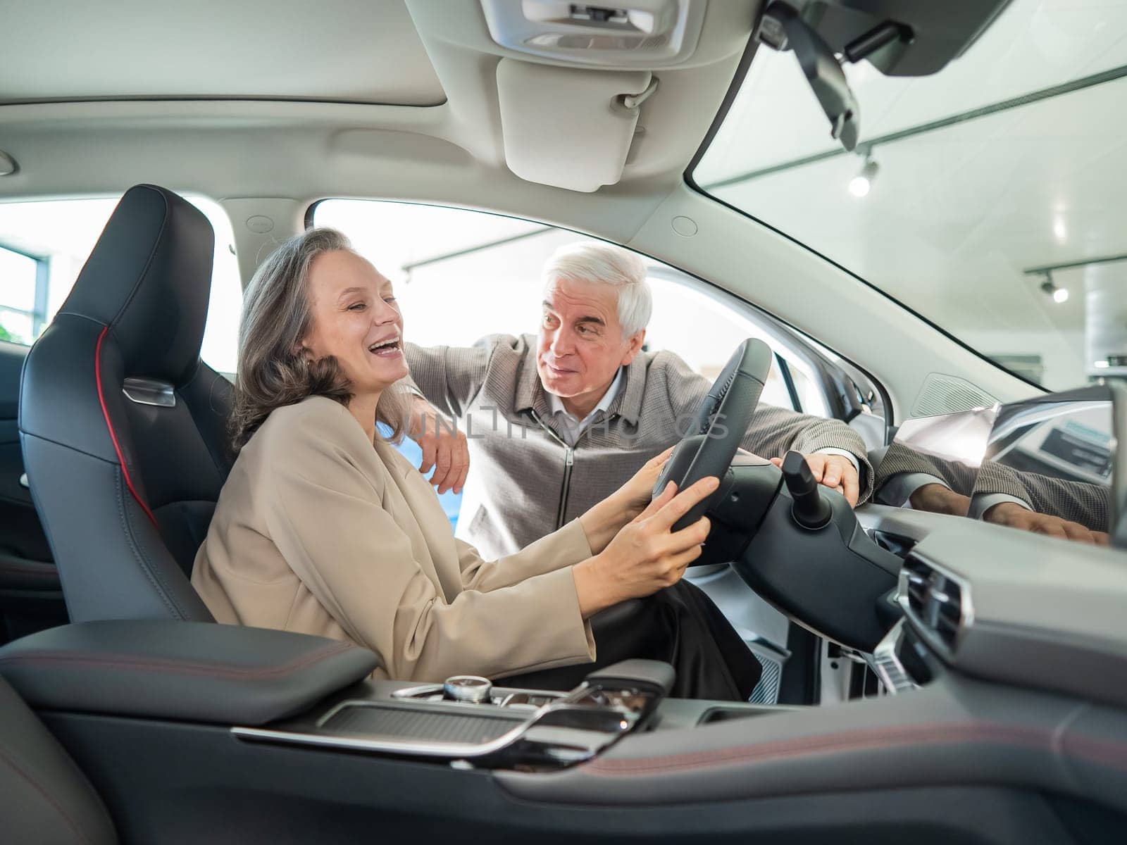 An elderly couple chooses a new car at a car dealership. Mature woman driving