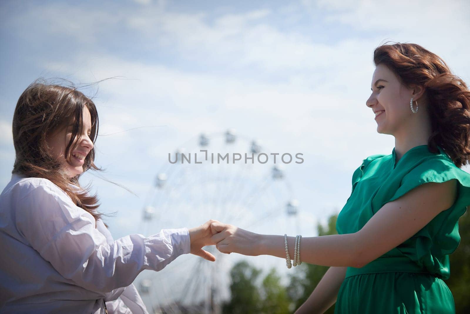 Happy Girls Enjoying Summer Day Together in the Park. Two young women stand on a platform in a park under a bright summer sky, smiling and relaxed