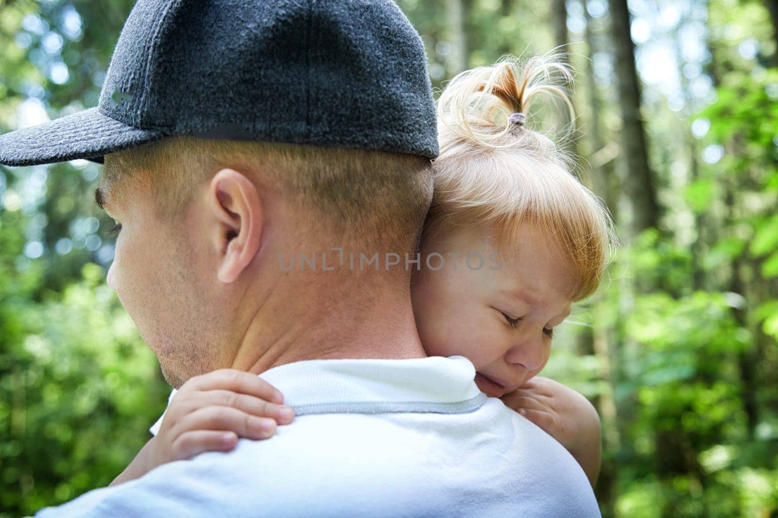 Gentle Father Holding Young Daughter Outdoors in Daylight. A tender moment as dad embraces his little girl in a sunny garden