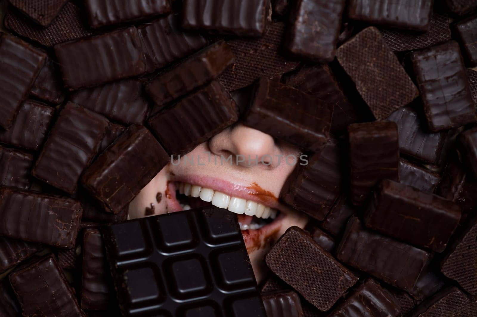 The face of a caucasian woman surrounded by chocolates. The girl eats a bar of chocolate. by mrwed54