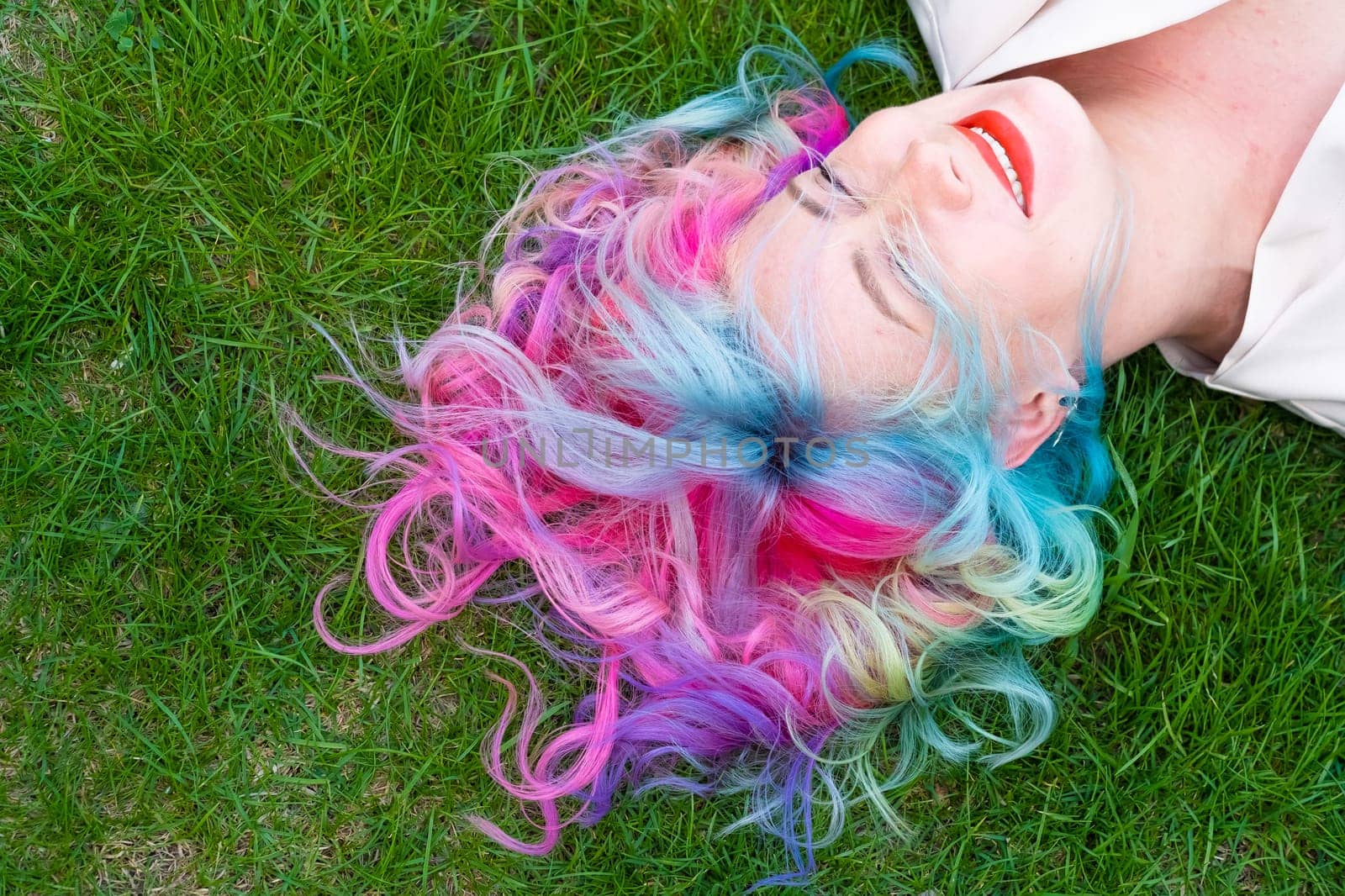 Top view of Caucasian woman with multi-colored hair lying on green grass