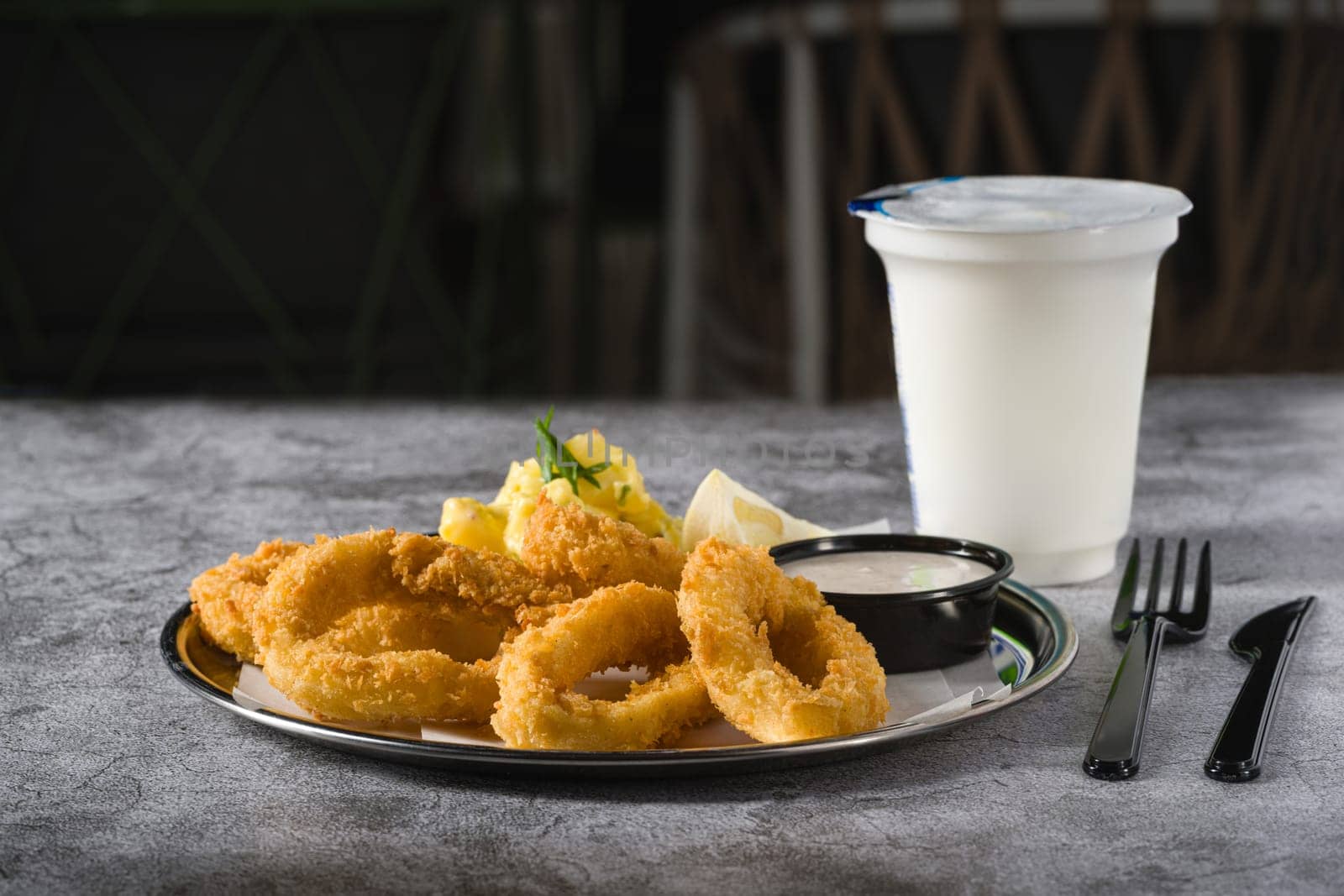 Fried calamari with potato salad next to it on stone table