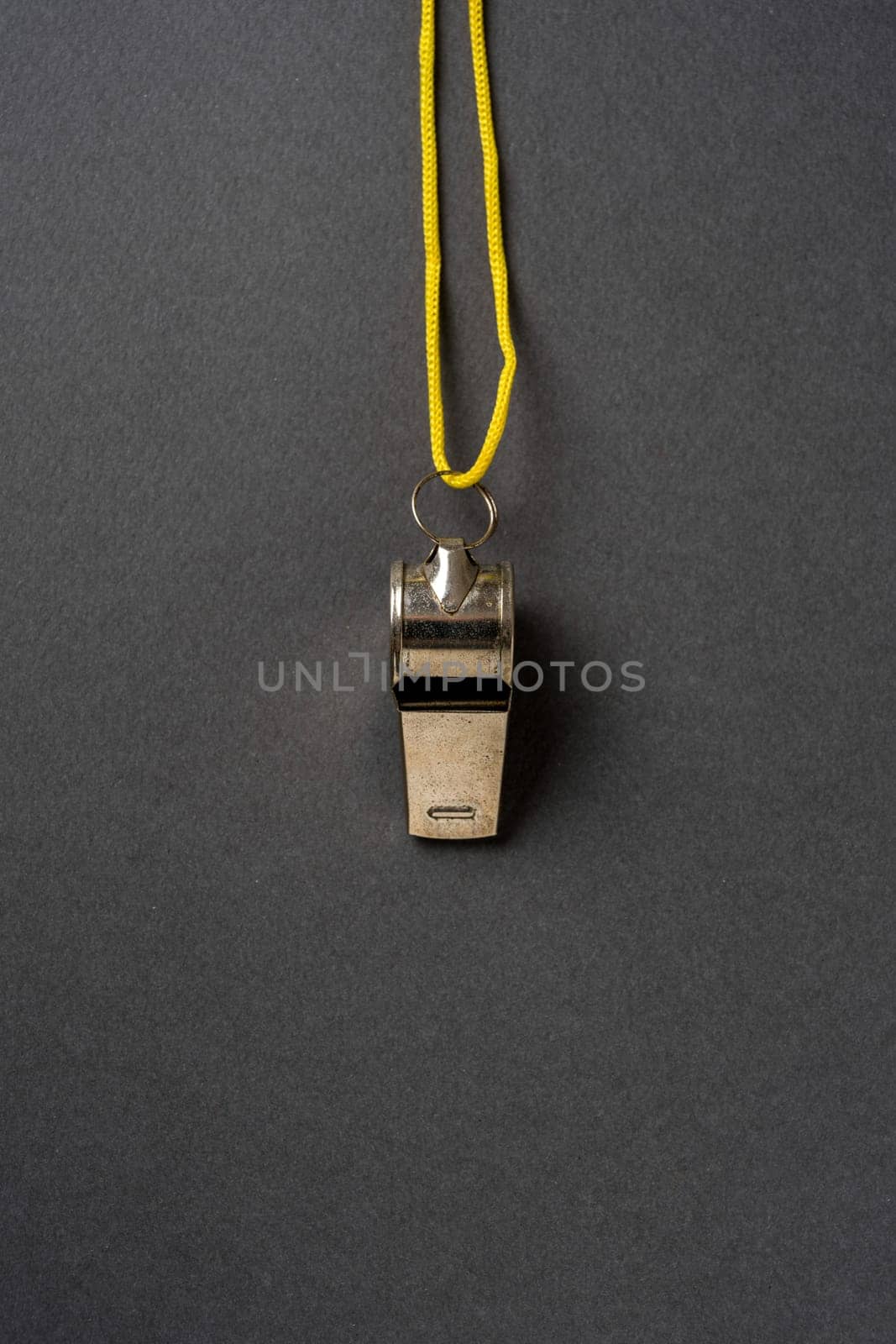 Top view of metal whistle with yellow string on dark gray background