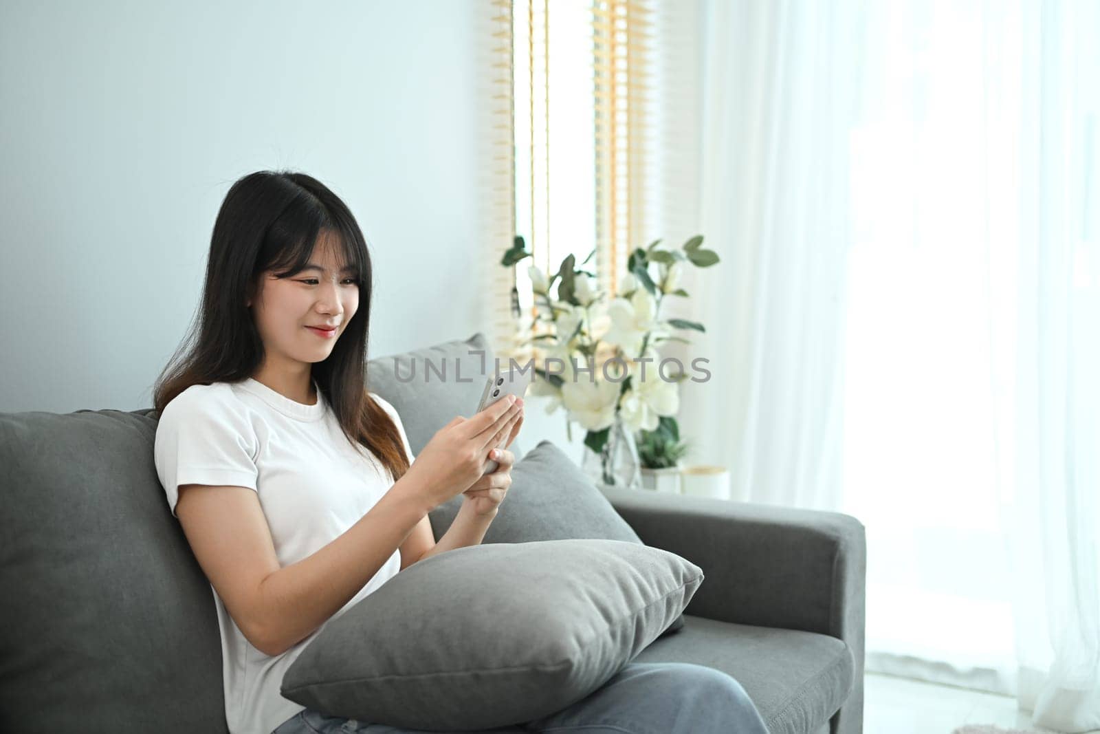 Beautiful young woman using smart phone for social media while sitting on couch.