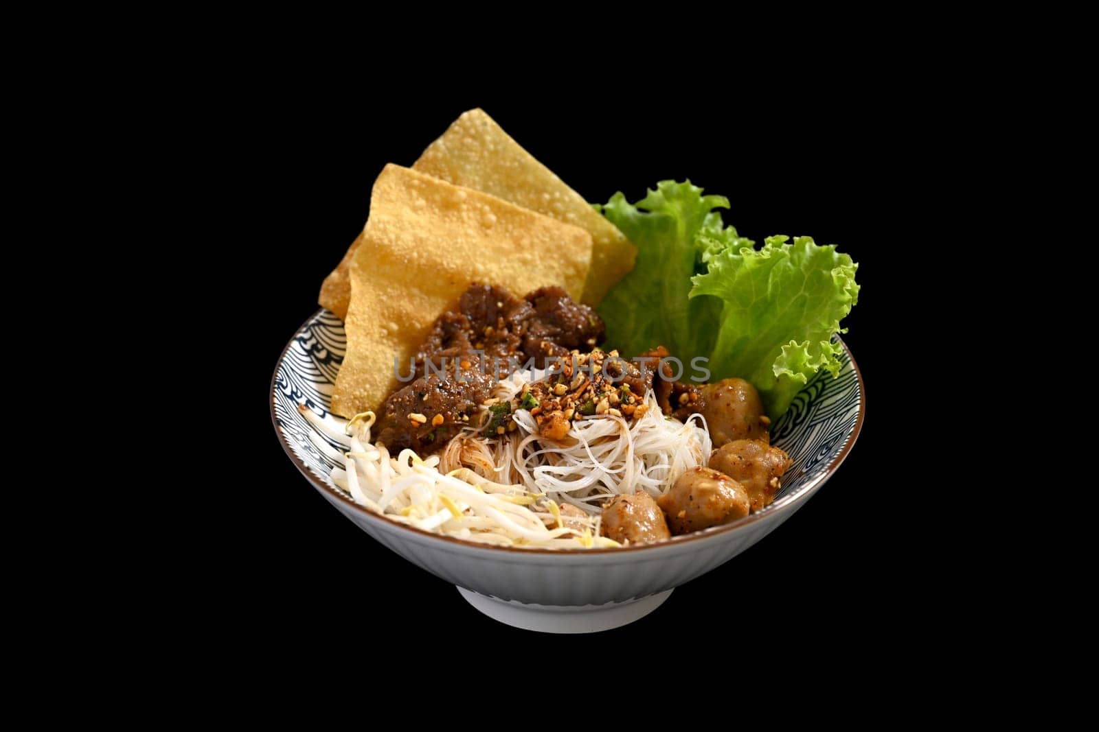 Rice noodles with sliced braised beef, meatballs and vegetables in a bowl on black background.