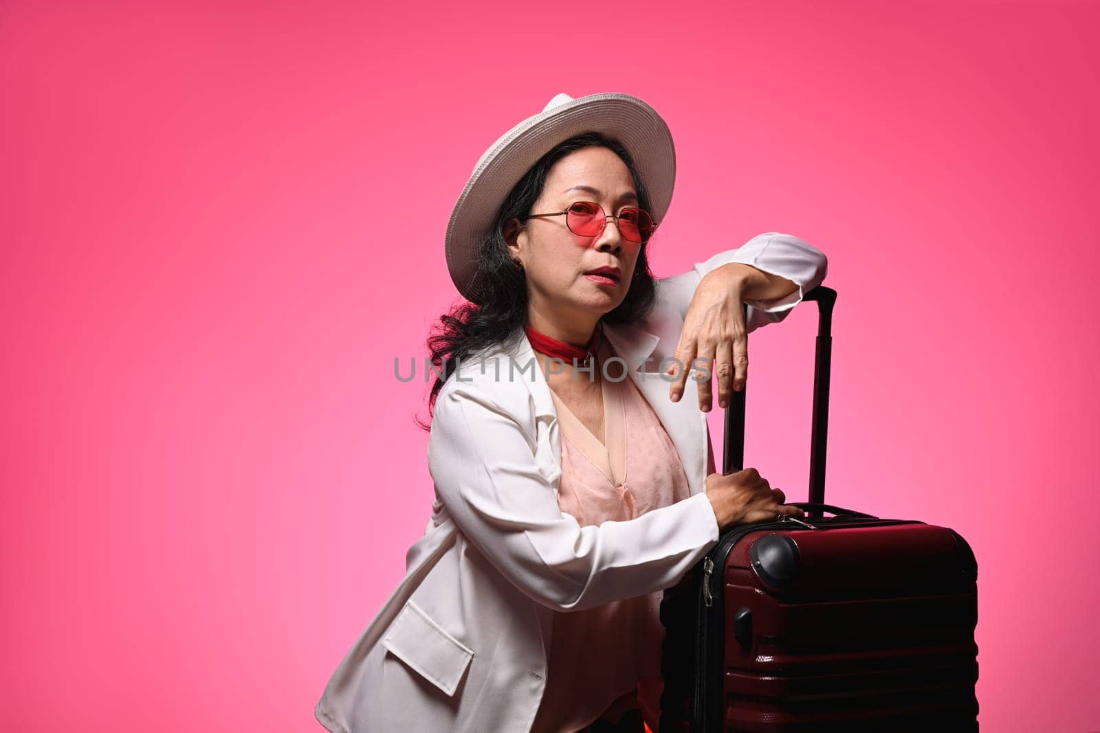 Beautiful senior woman tourist with travel bag standing on pink background. Summer, travel and vacation concept.