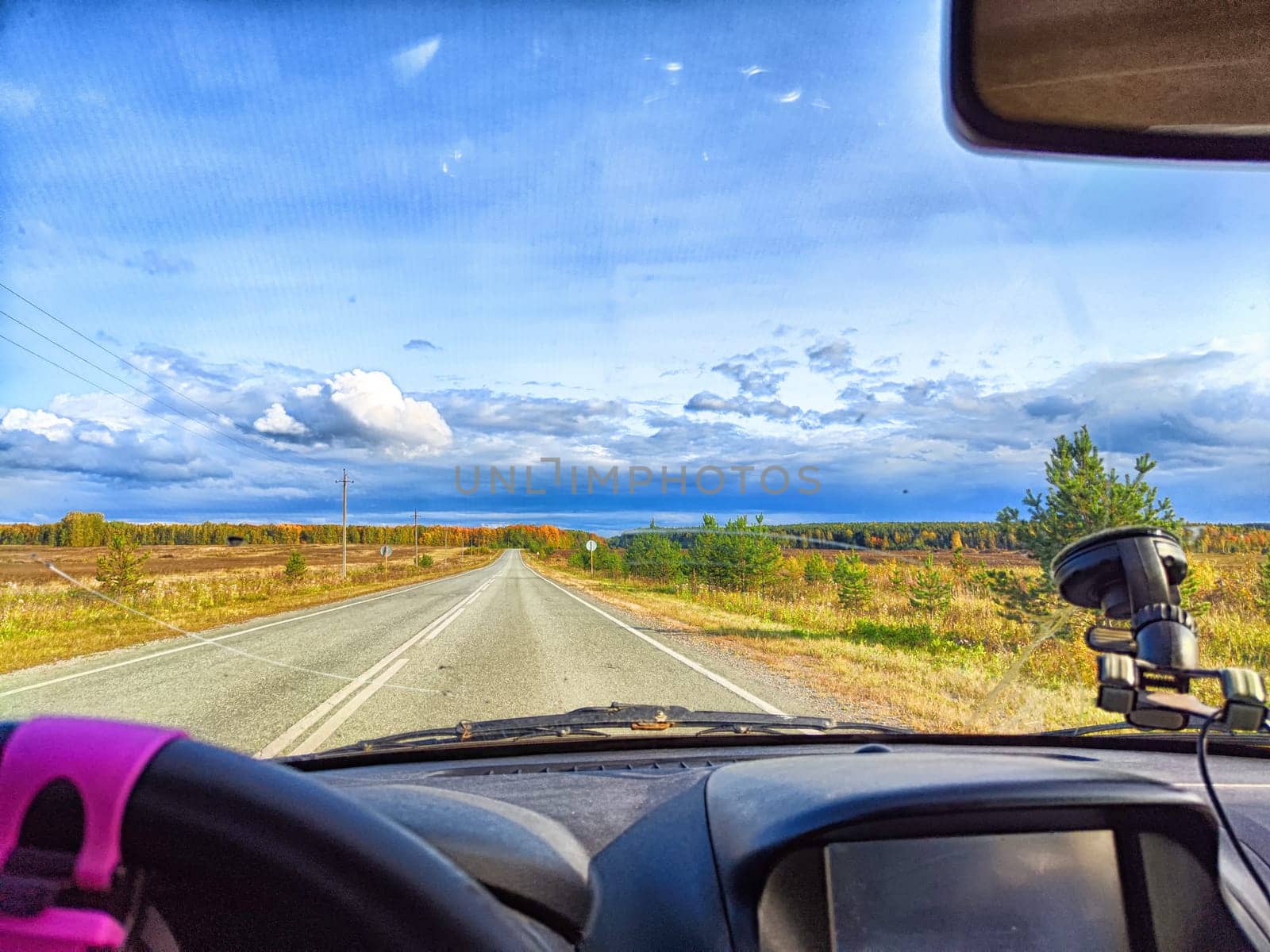Car salon, windshield, hand on steering wheel and landscape in sunny day. View from driver on nature and Road. Single traveler. Partial focus. Blurred