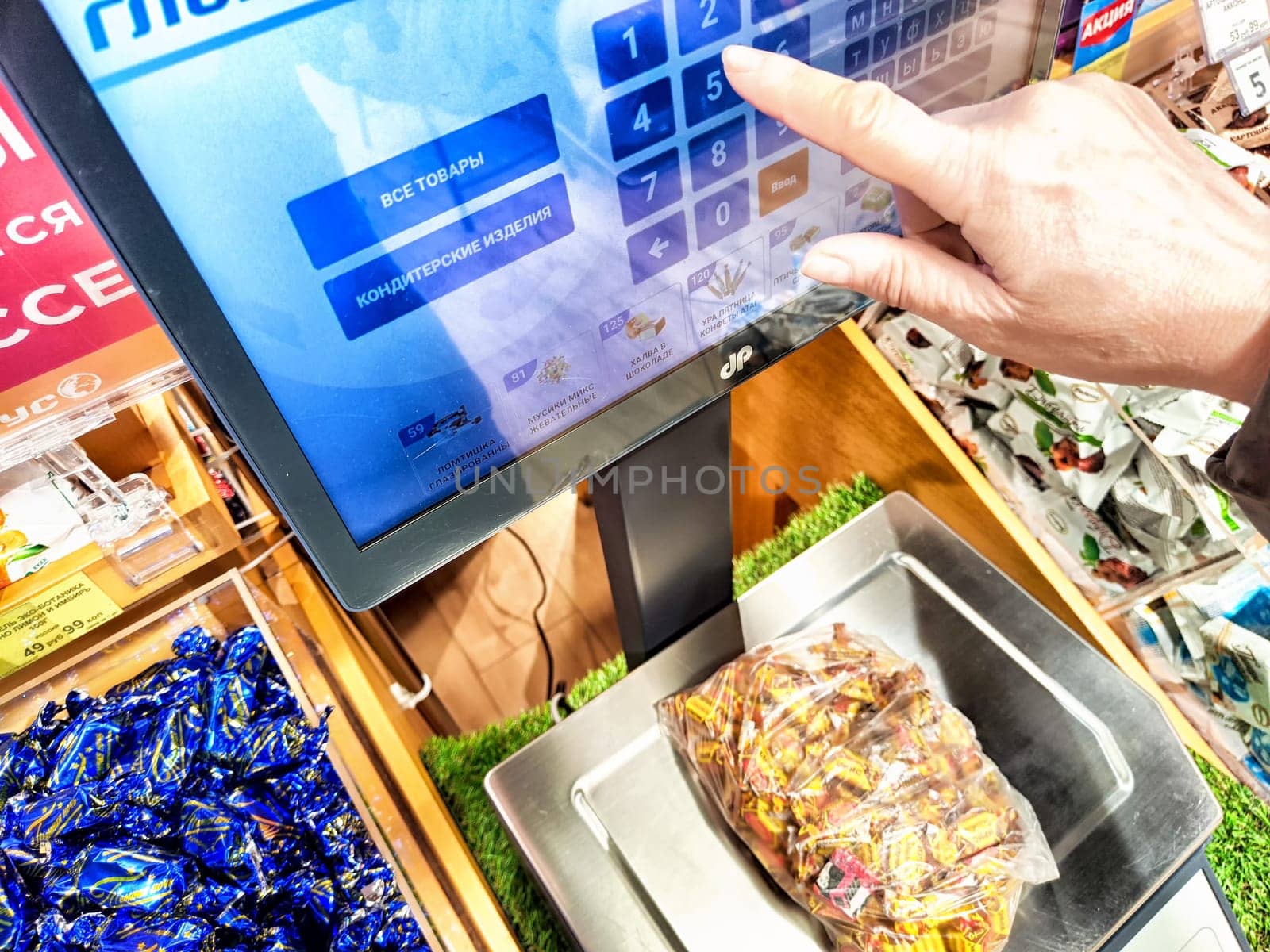 Kirov, Russia - April 17, 2024: Customer Weighing Produce on Digital Scales at Grocery Store. A person is using a touchscreen to weigh items at store