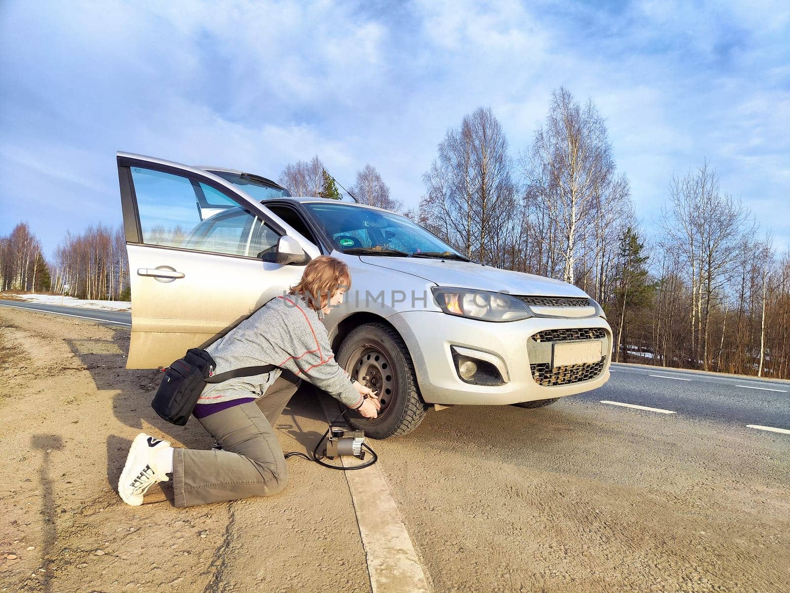 A girl repairs a car wheel on the road. The concept of car travel. A woman repairs car wheel on a sunny roadside