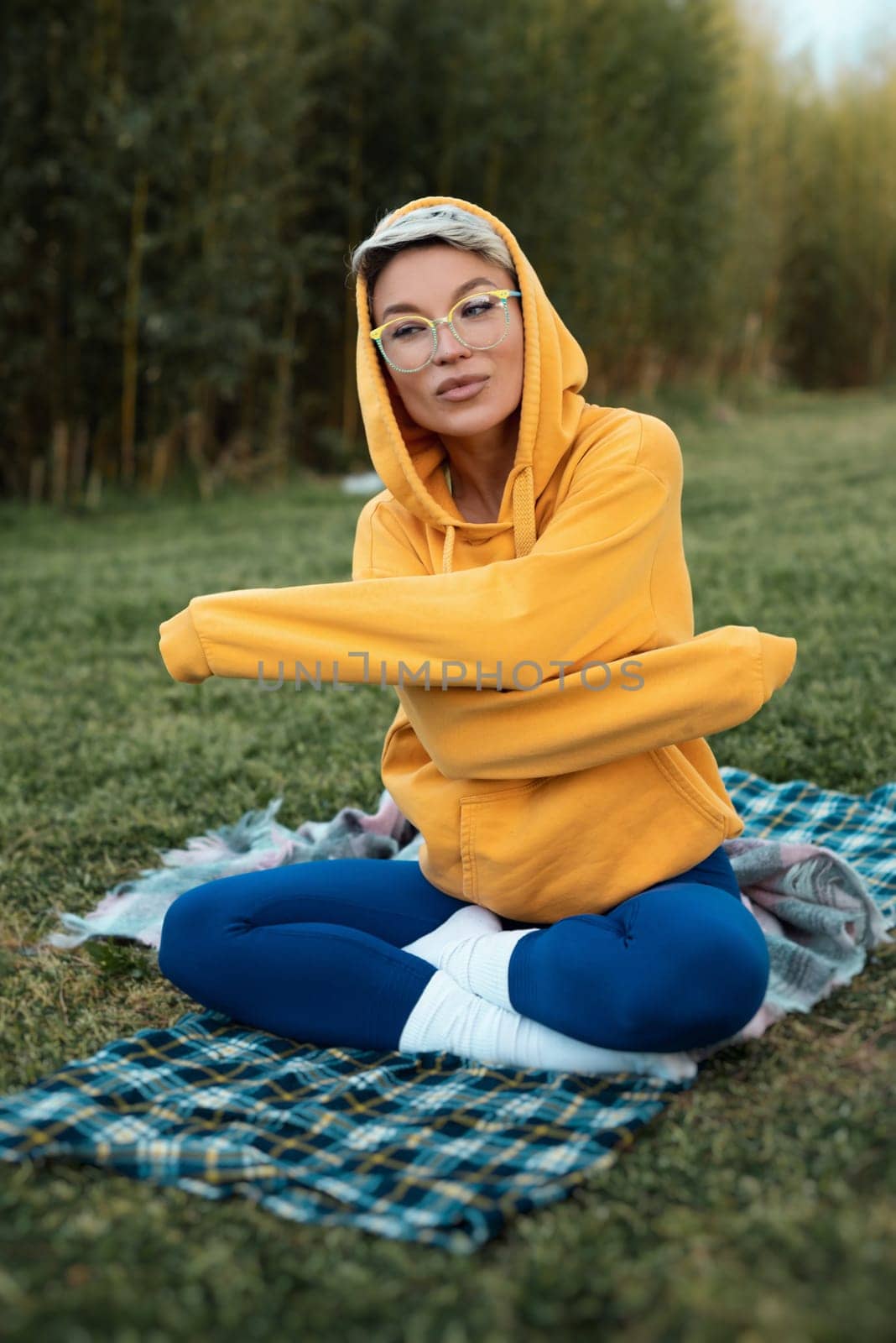 A cute girl with glasses in an orange hoodie is sitting in a park in nature expressing kind emotions