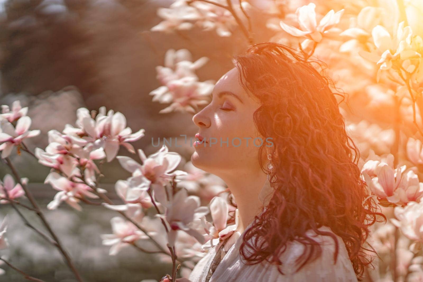 Magnolia park woman. Stylish woman in a hat stands near the magnolia bush in the park. Dressed in white corset pants and posing for the camera. by Matiunina