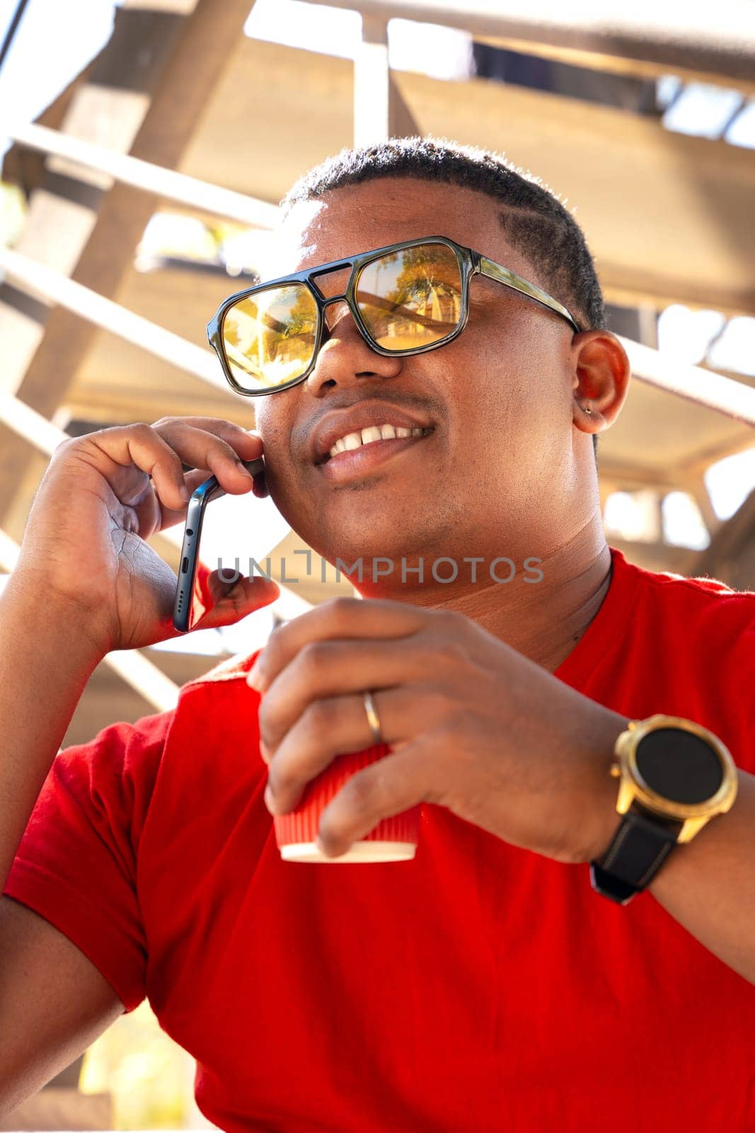 Vertical portrait black man talking on cell Phone and drinking coffee smiling by mariaphoto3