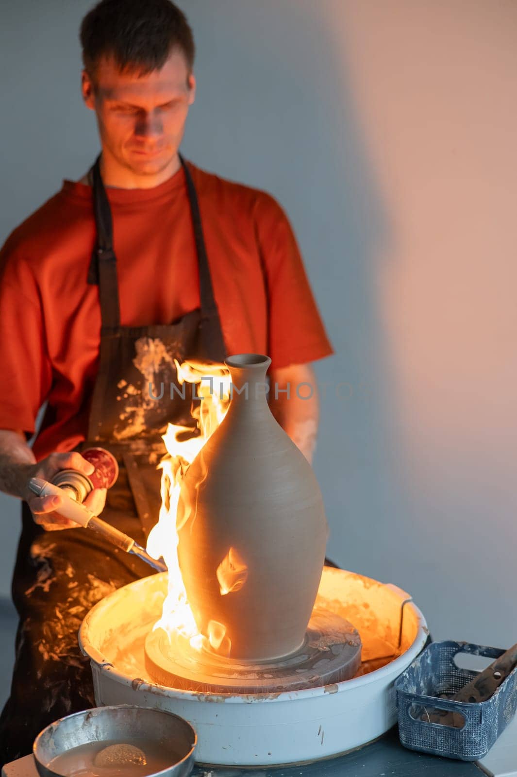 A potter burns a jug with a gas burner on a potter's wheel. Vertical photo