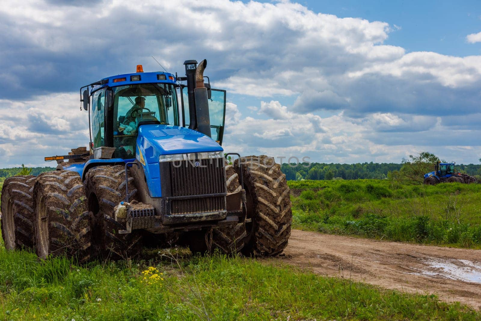 Blue New Holland tractor with double wheels standing near agricultural field at hot sunny day in Tula, Russia - June 4, 2022