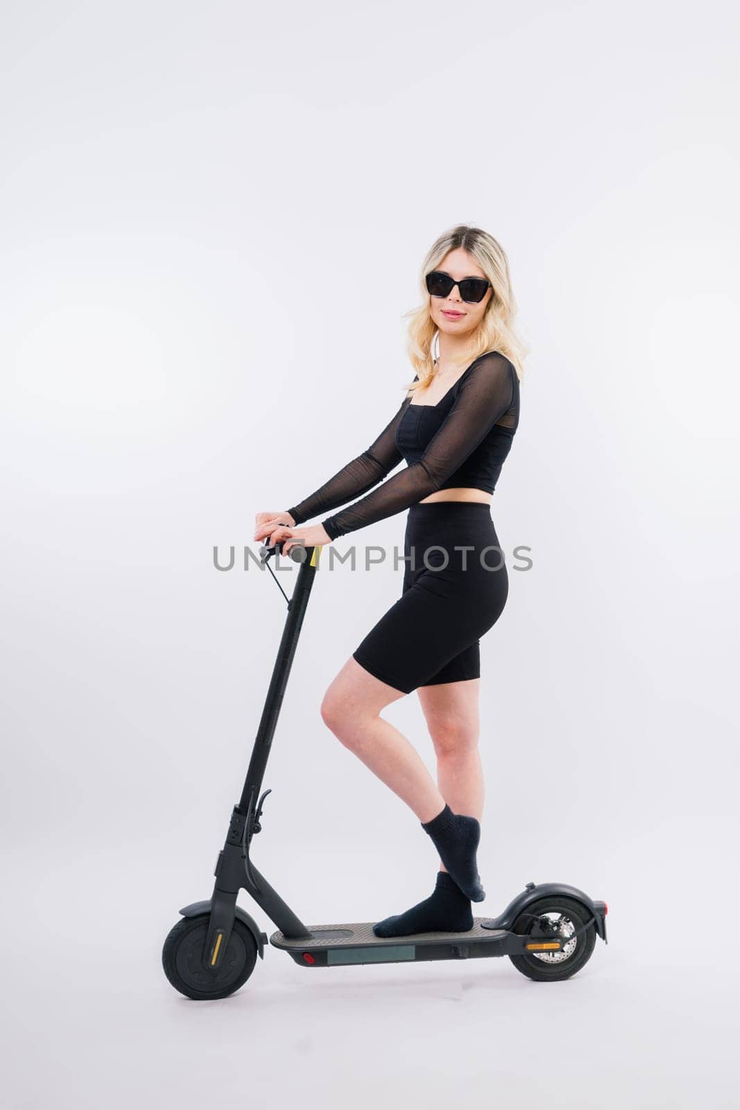 Beautiful emotional young female in sport clothes on electric scooter on red and white background by Zelenin