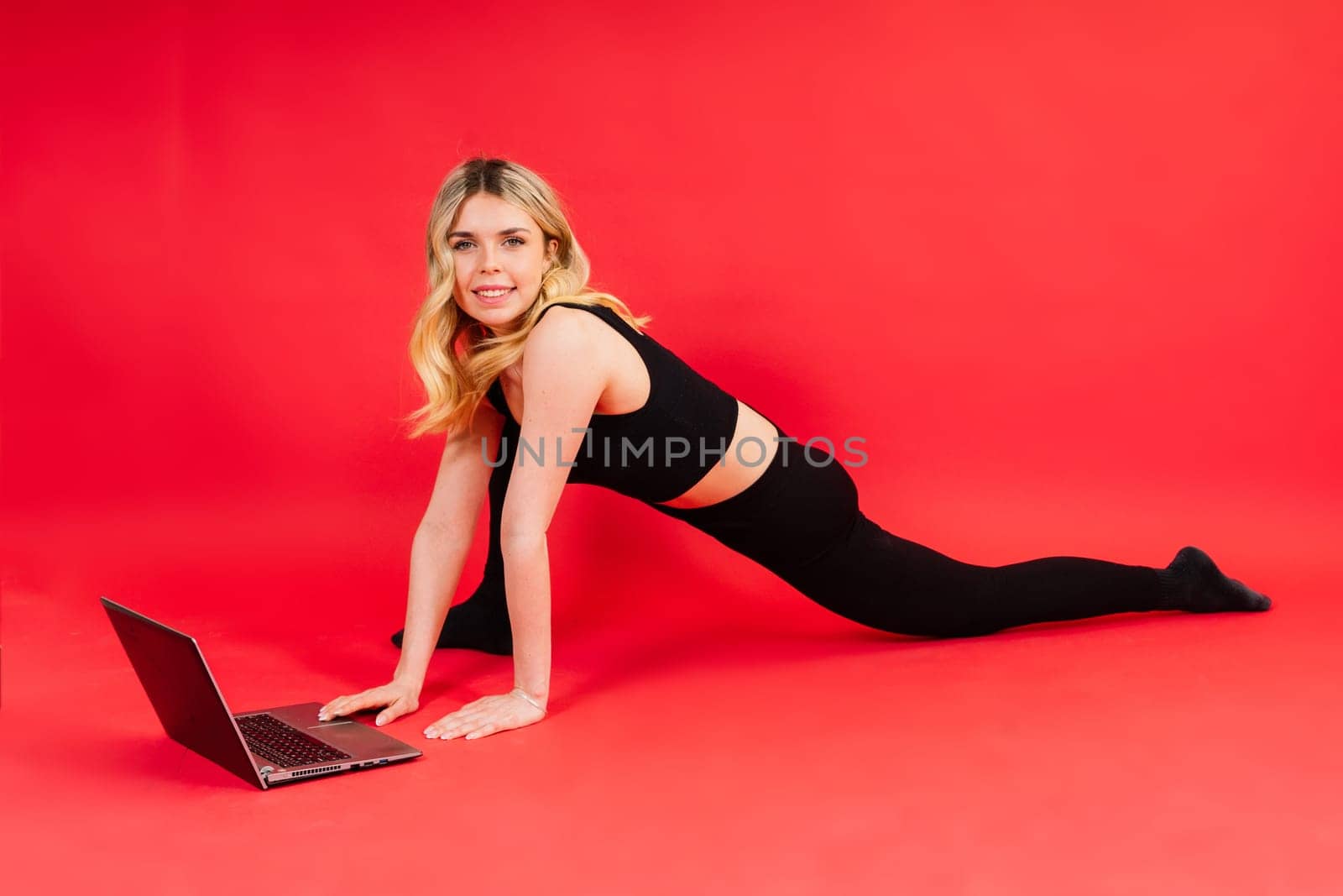 Fit woman doing stretching exercise and watching meditation video on a laptop in studio.