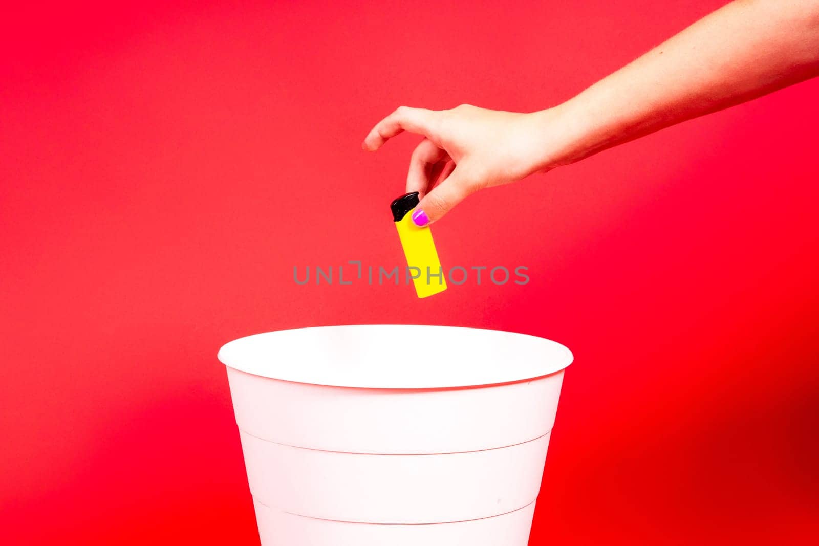 The old lighter is thrown into a trash basket. Red background, selective focus, copy space.