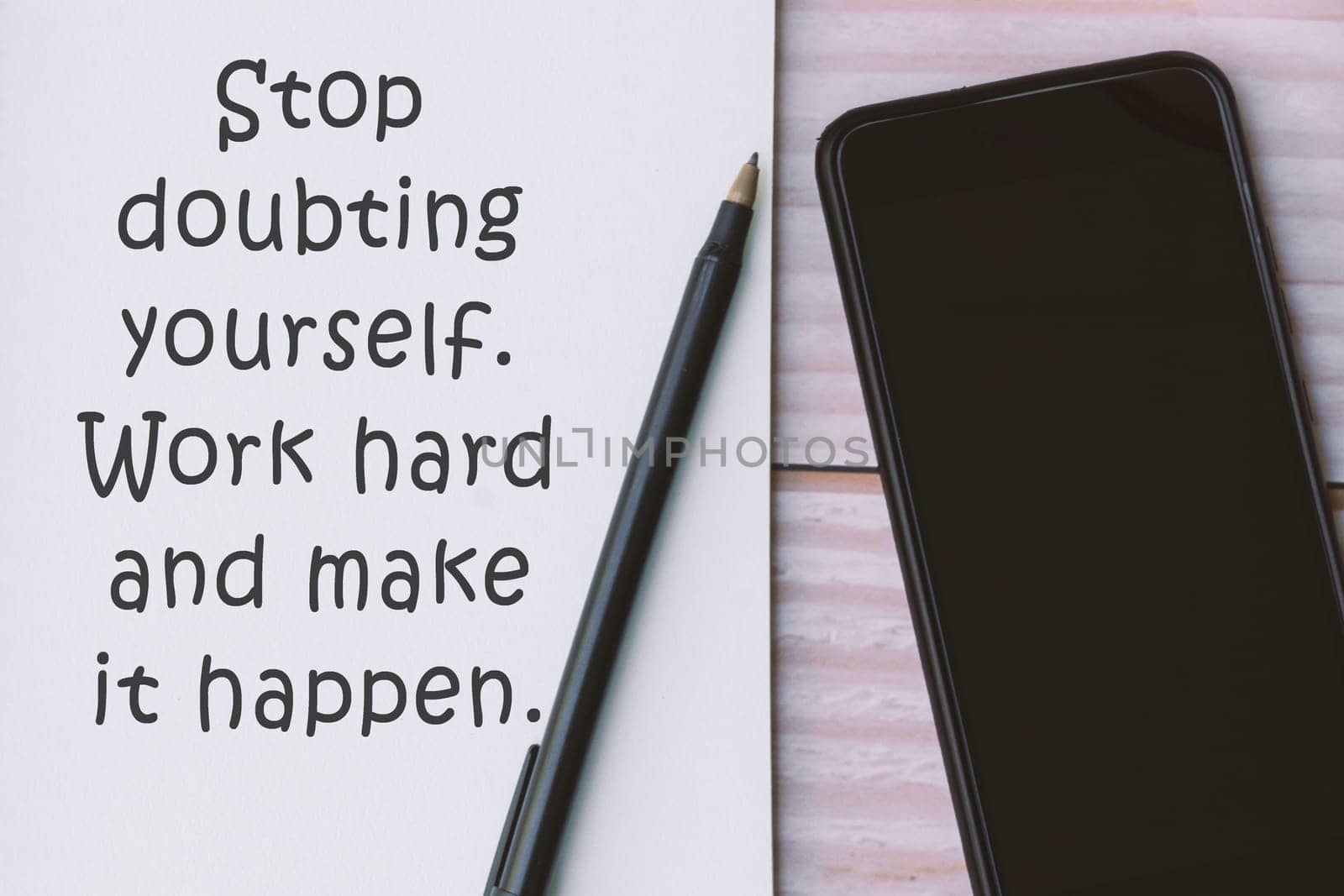 Motivational quote written on notebook with pen and smartphone on wooden background - Stop doubting yourself. Work hard and make it happen.