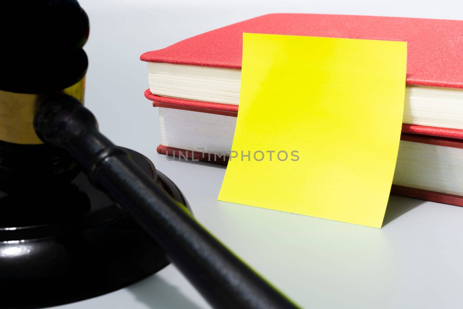 Judge's gavel with yellow note and red books on white background. Copy space.