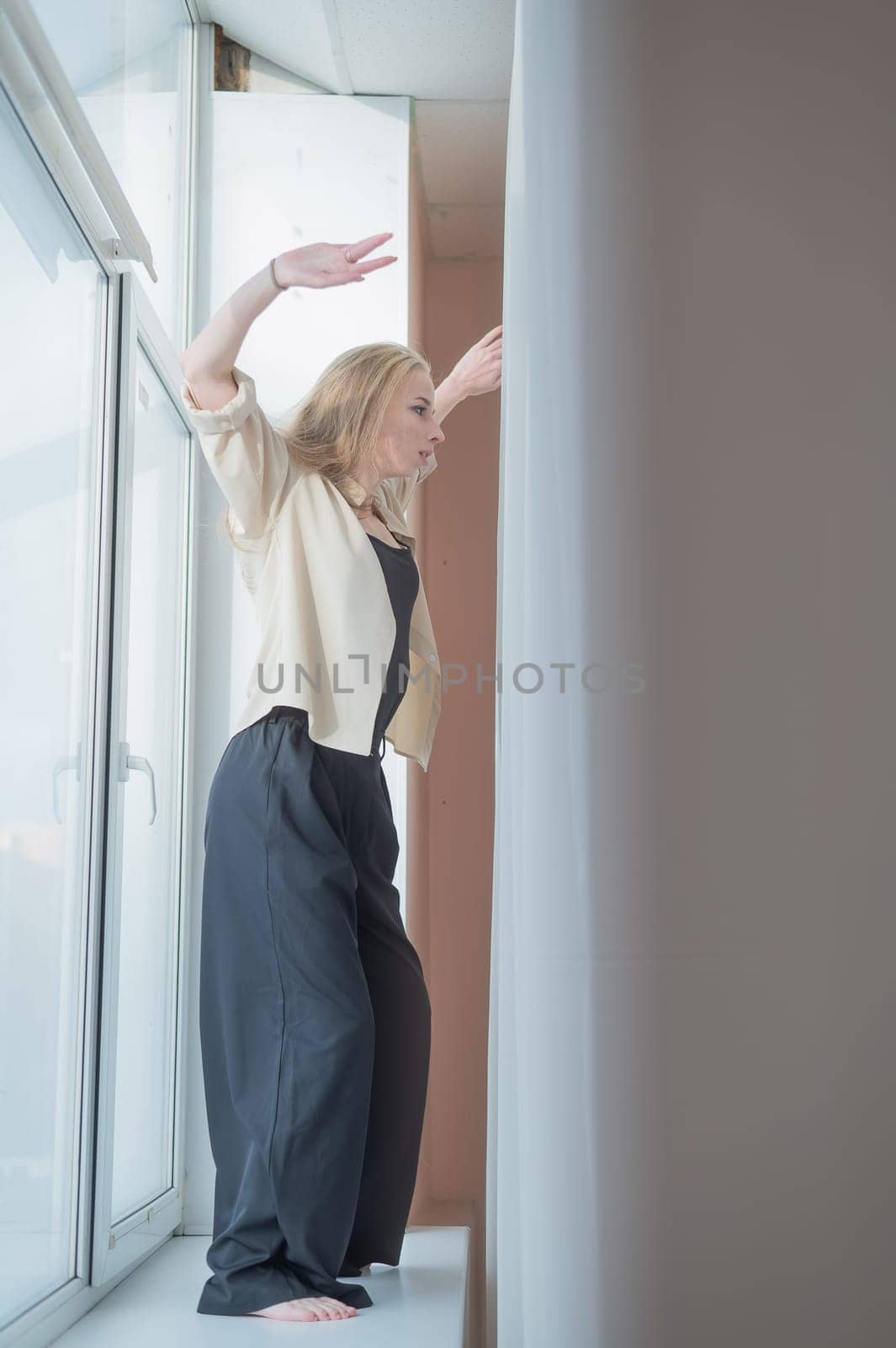 Caucasian woman dancing modern dance on the windowsill. Vertical photo