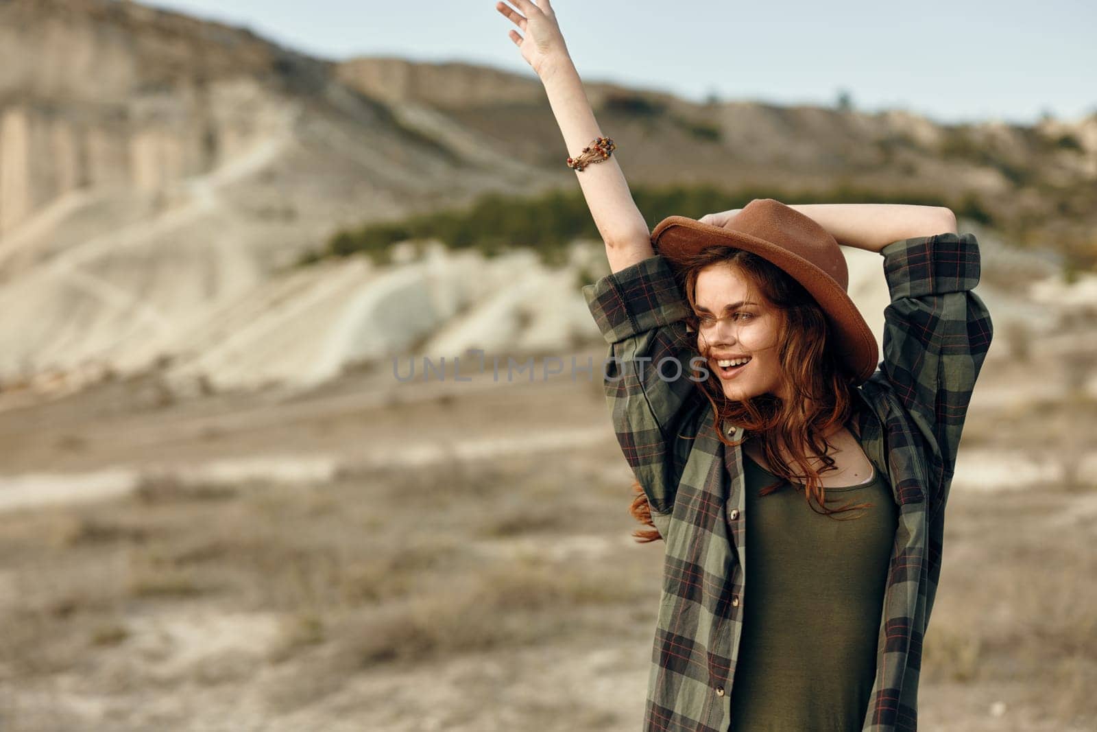 empowered woman in plaid shirt and hat raises arms triumphantly in the vast desert landscape by Vichizh