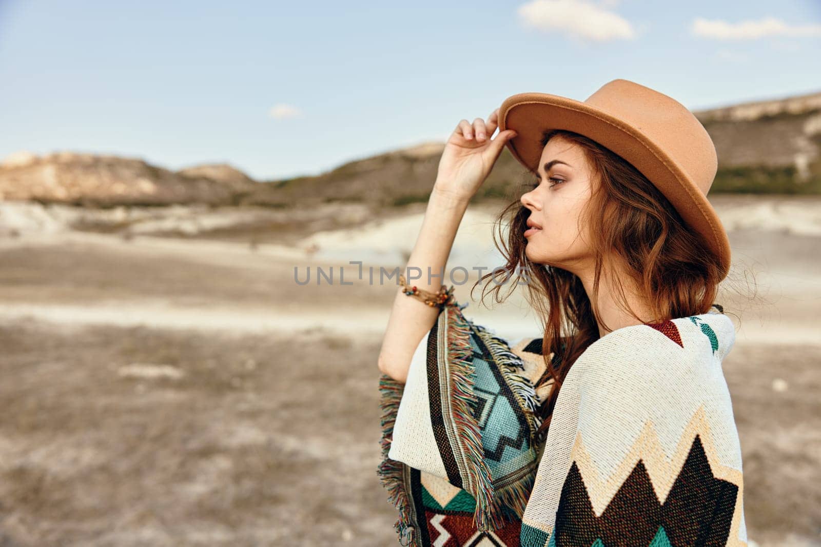 Woman in stylish hat and poncho standing confidently in vast desert landscape