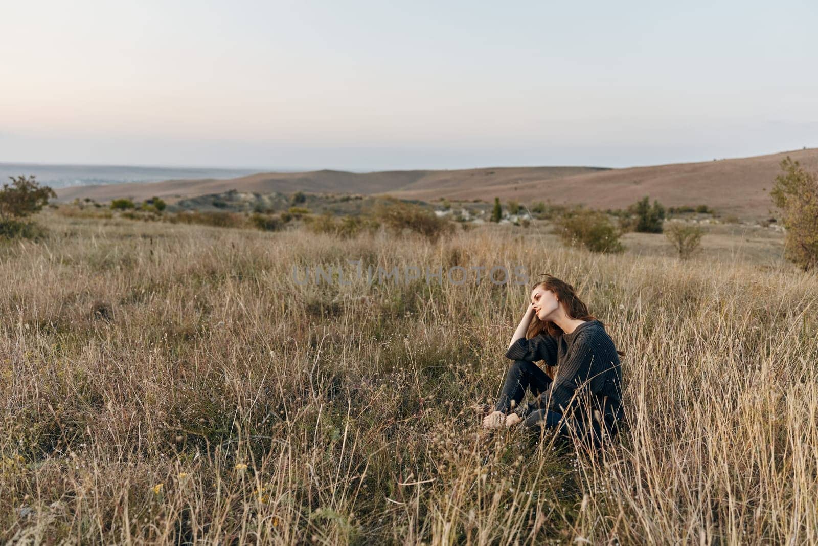 Solitary woman enjoys peaceful sunset in desert hill surrounded by tall grass by Vichizh