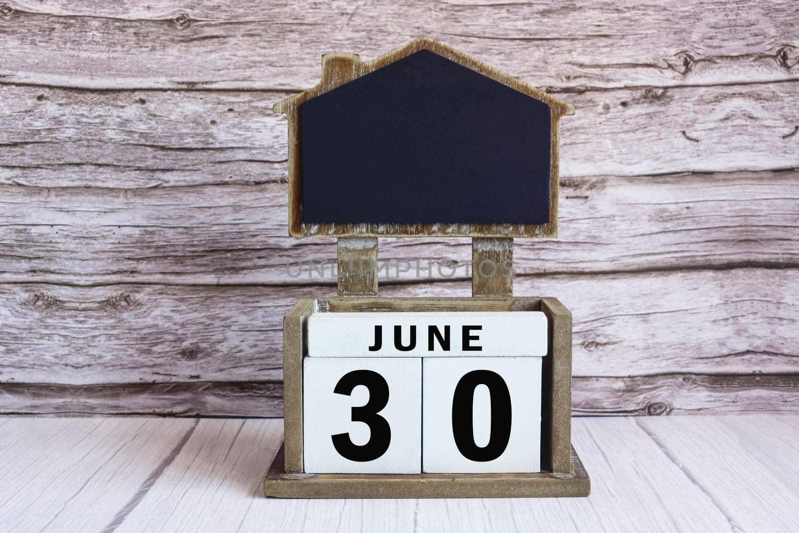Chalkboard with June 30 calendar date on white cube block on wooden table.