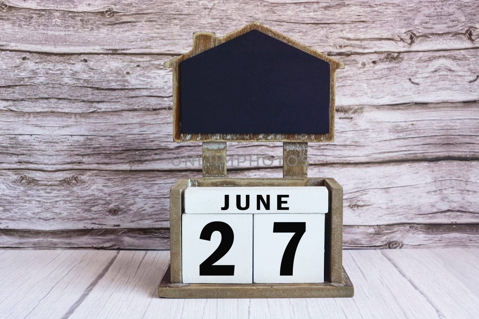 Chalkboard with June 27 calendar date on white cube block on wooden table.